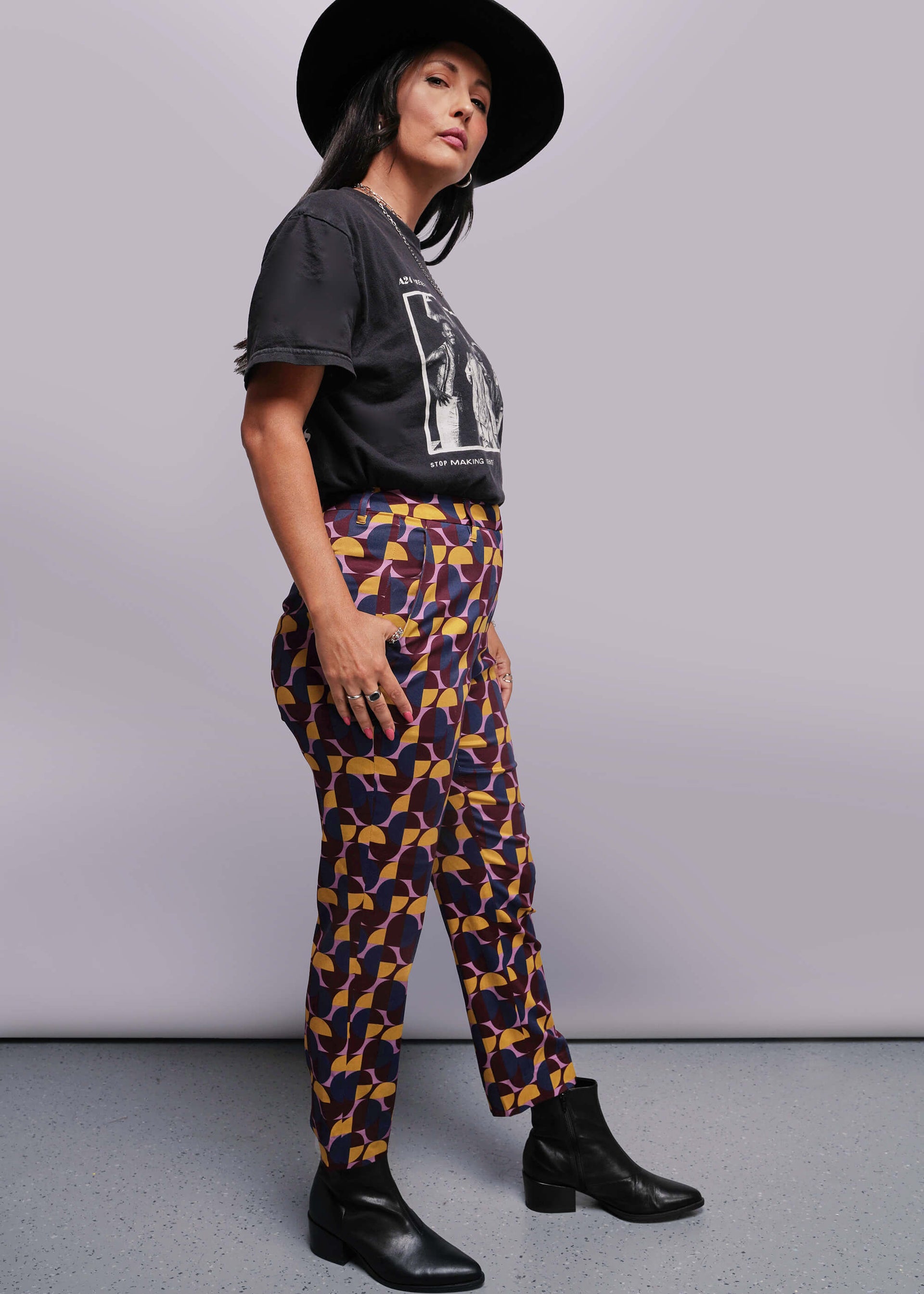 S=Woman wearing a black t-shirt and patterned pants against a gray background