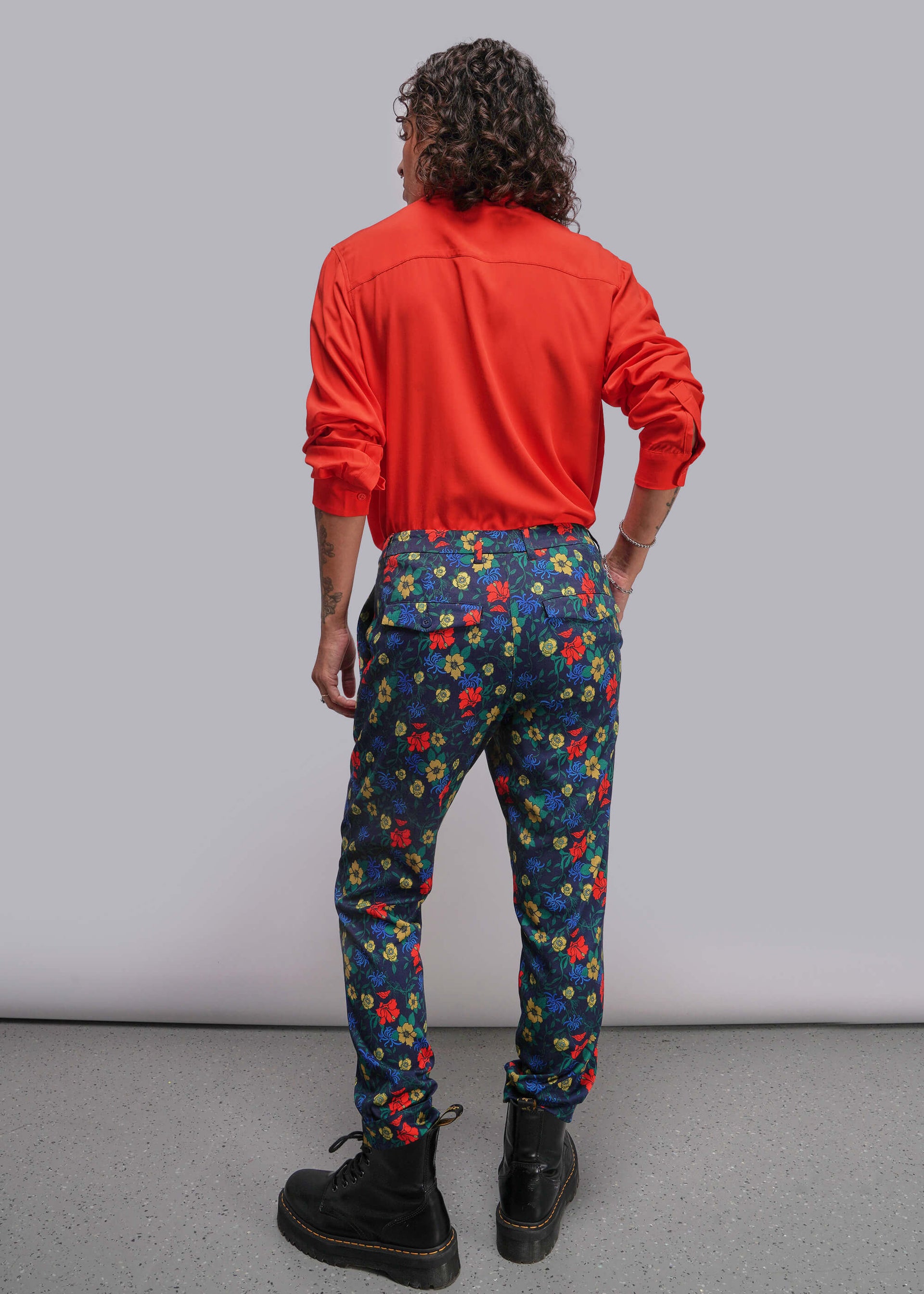 S=Person wearing a red jacket and colorful floral pants against a gray background