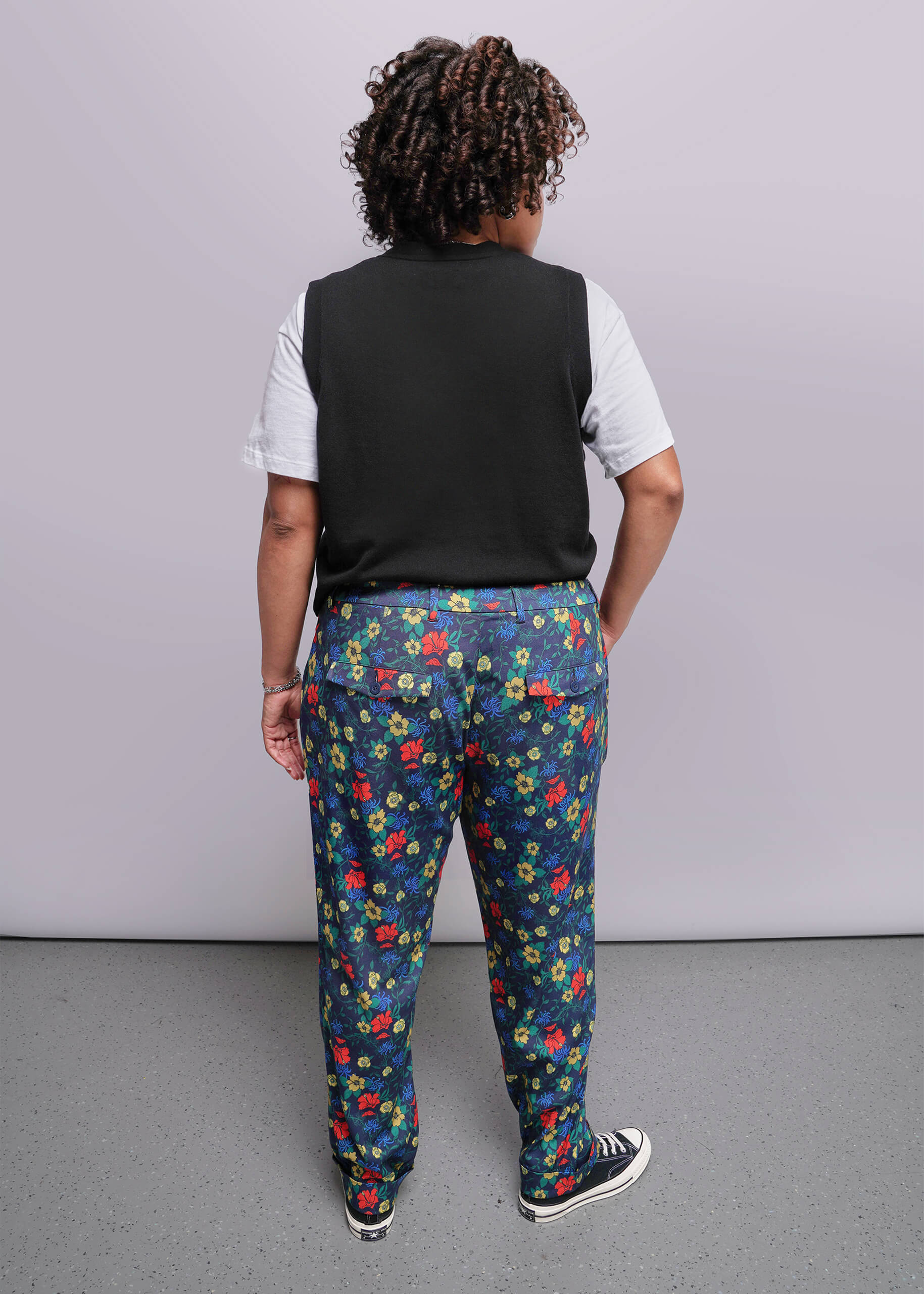 1X=Person wearing a black vest, white shirt, and colorful floral pants against a plain background