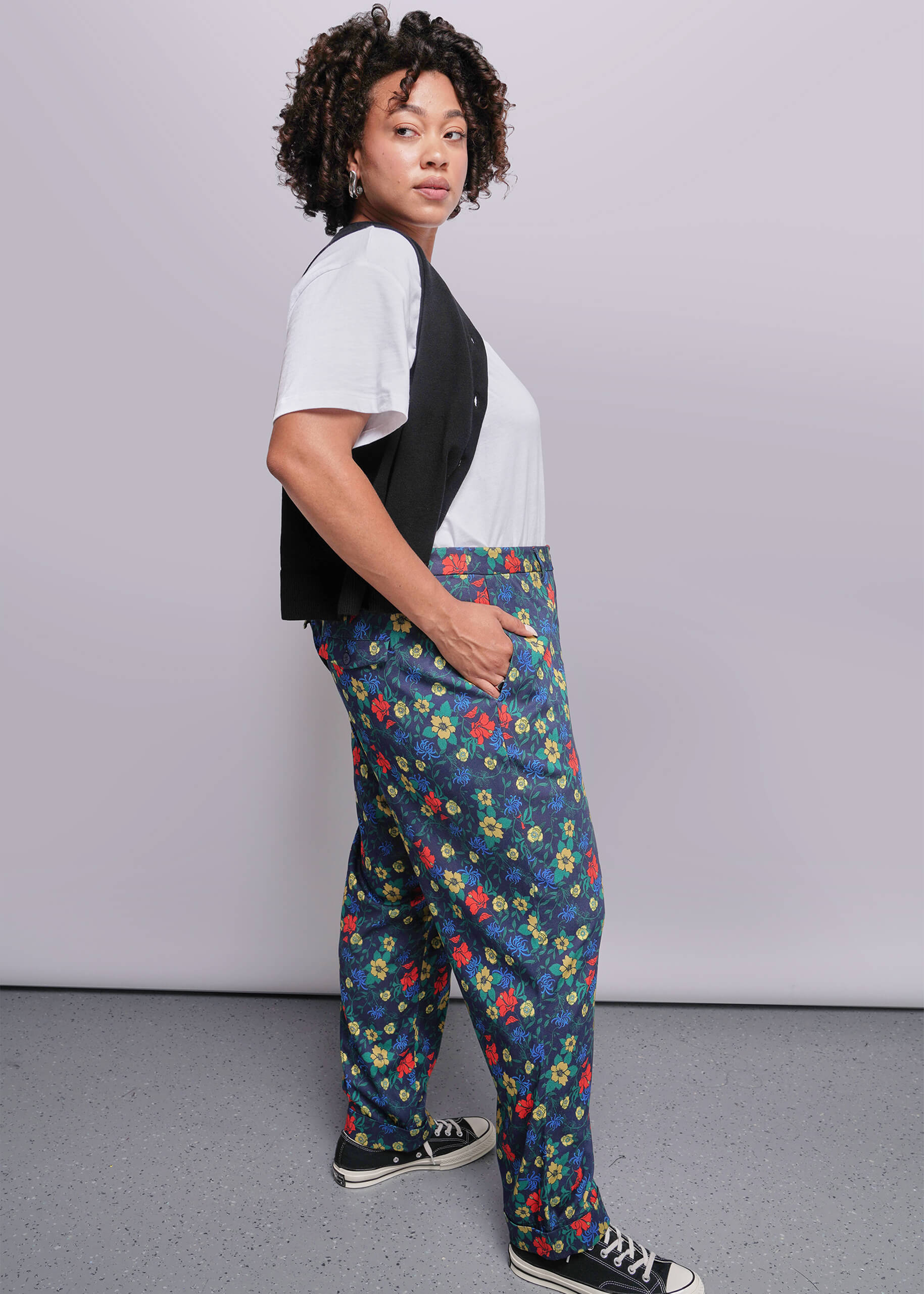 1X=Person wearing a white and black top with colorful floral pants against a plain background