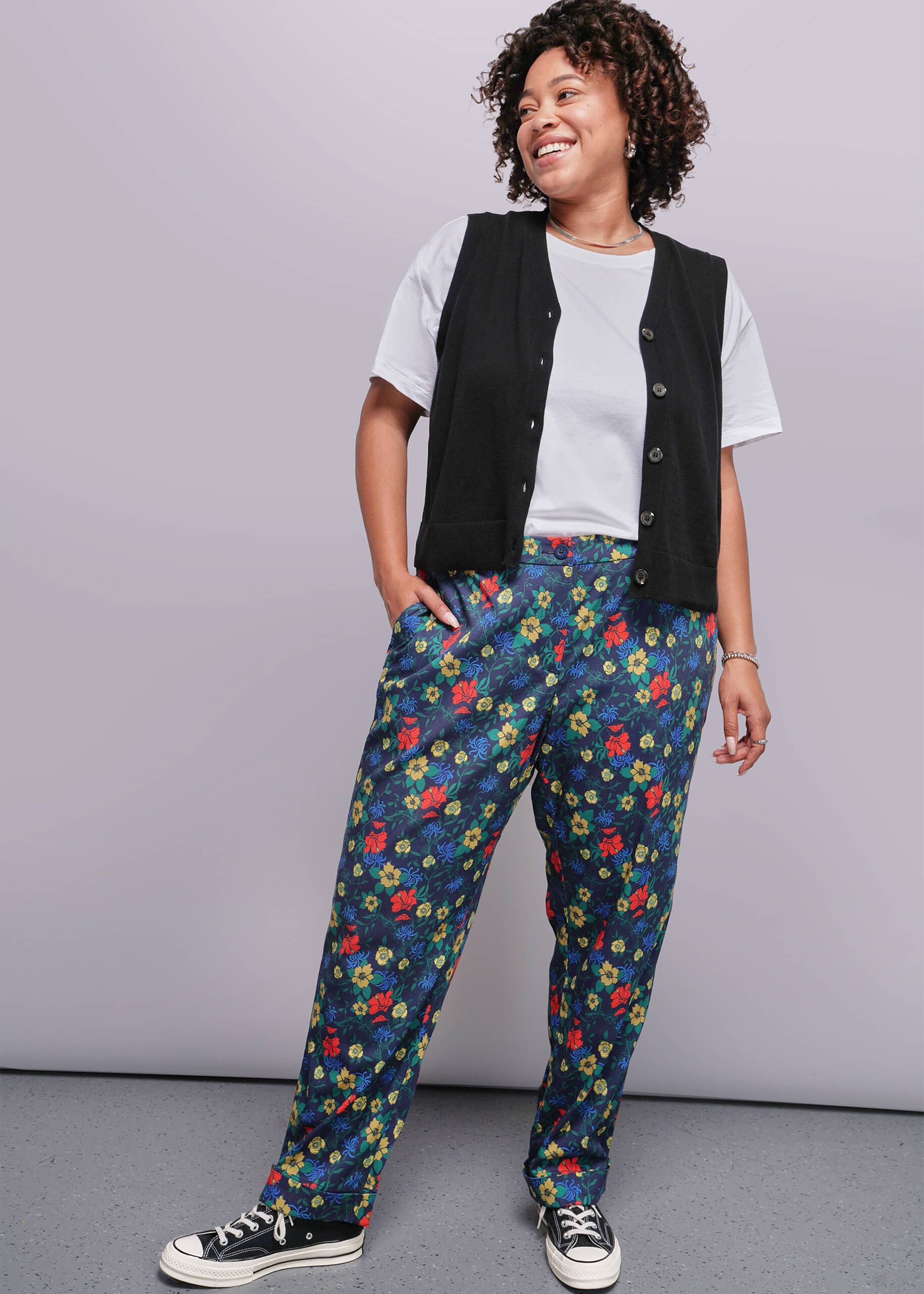 1X=Person wearing a black vest, white shirt, and colorful floral pants against a gray background