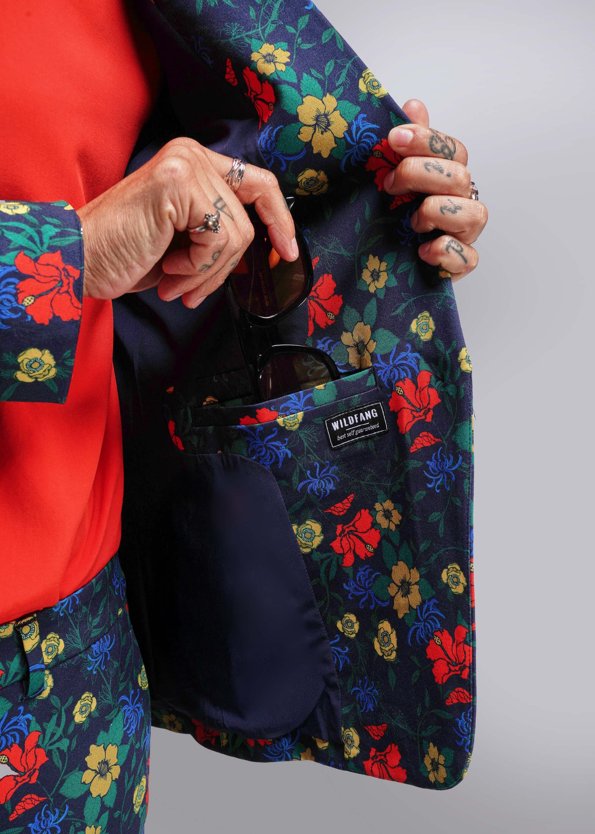 S=Person holding a floral-patterned jacket with a visible brand label.