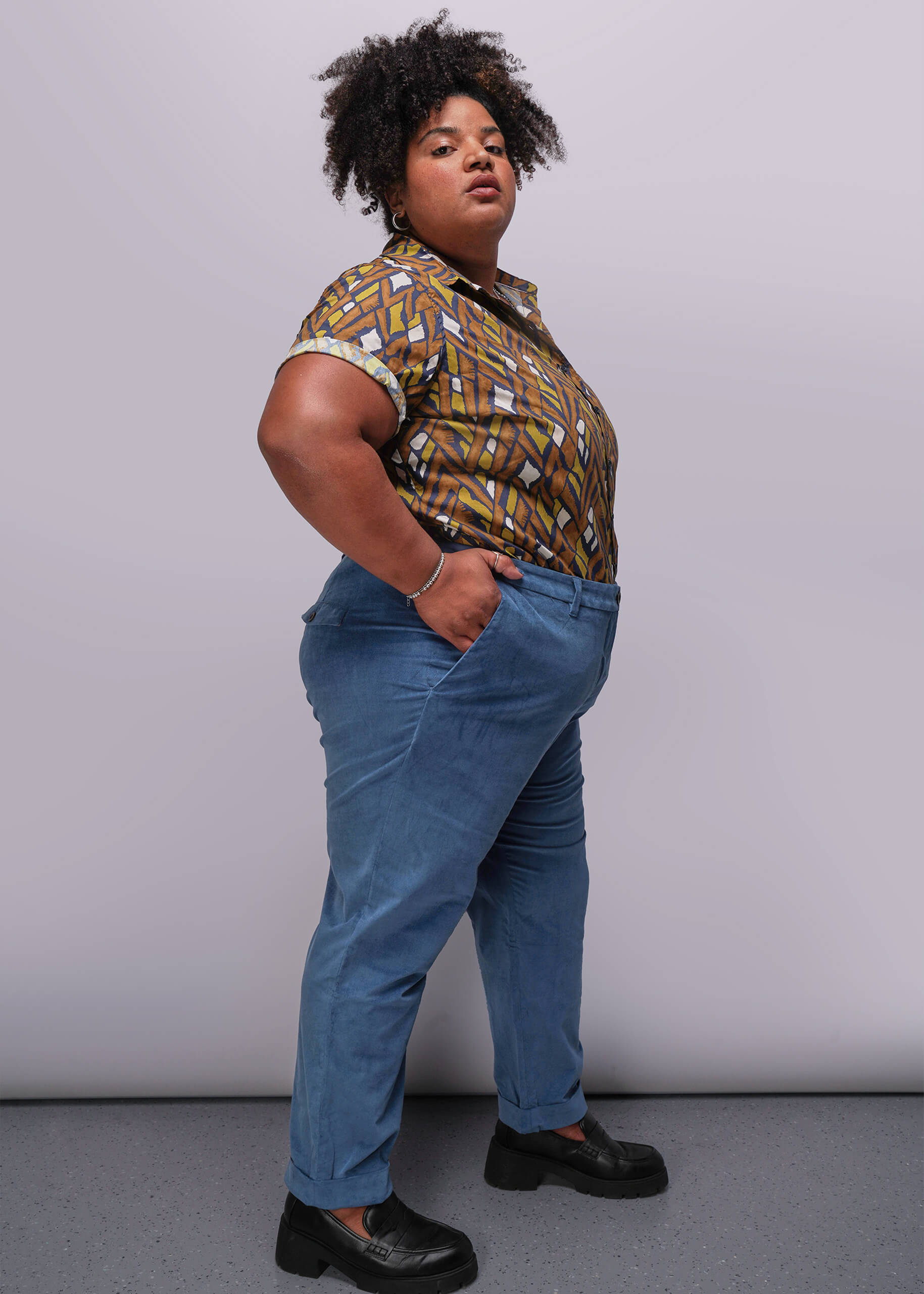 1X=Person wearing a patterned shirt and blue jeans against a plain background