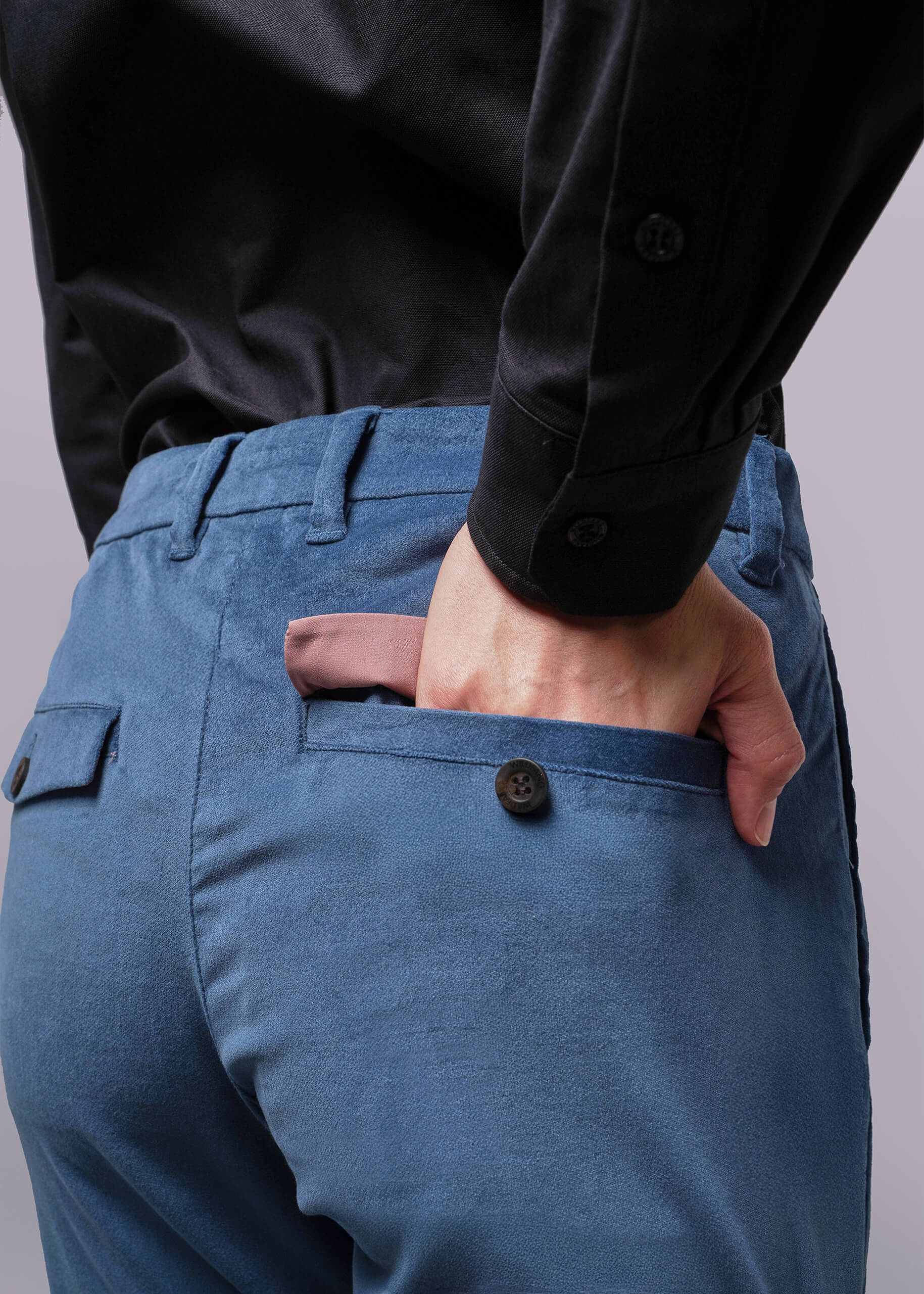 S=Person wearing blue pants and a black shirt with one hand in the pocket against a gray background
