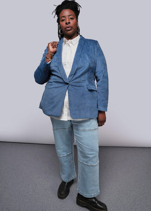 1X=Person wearing a blue blazer and jeans against a plain background