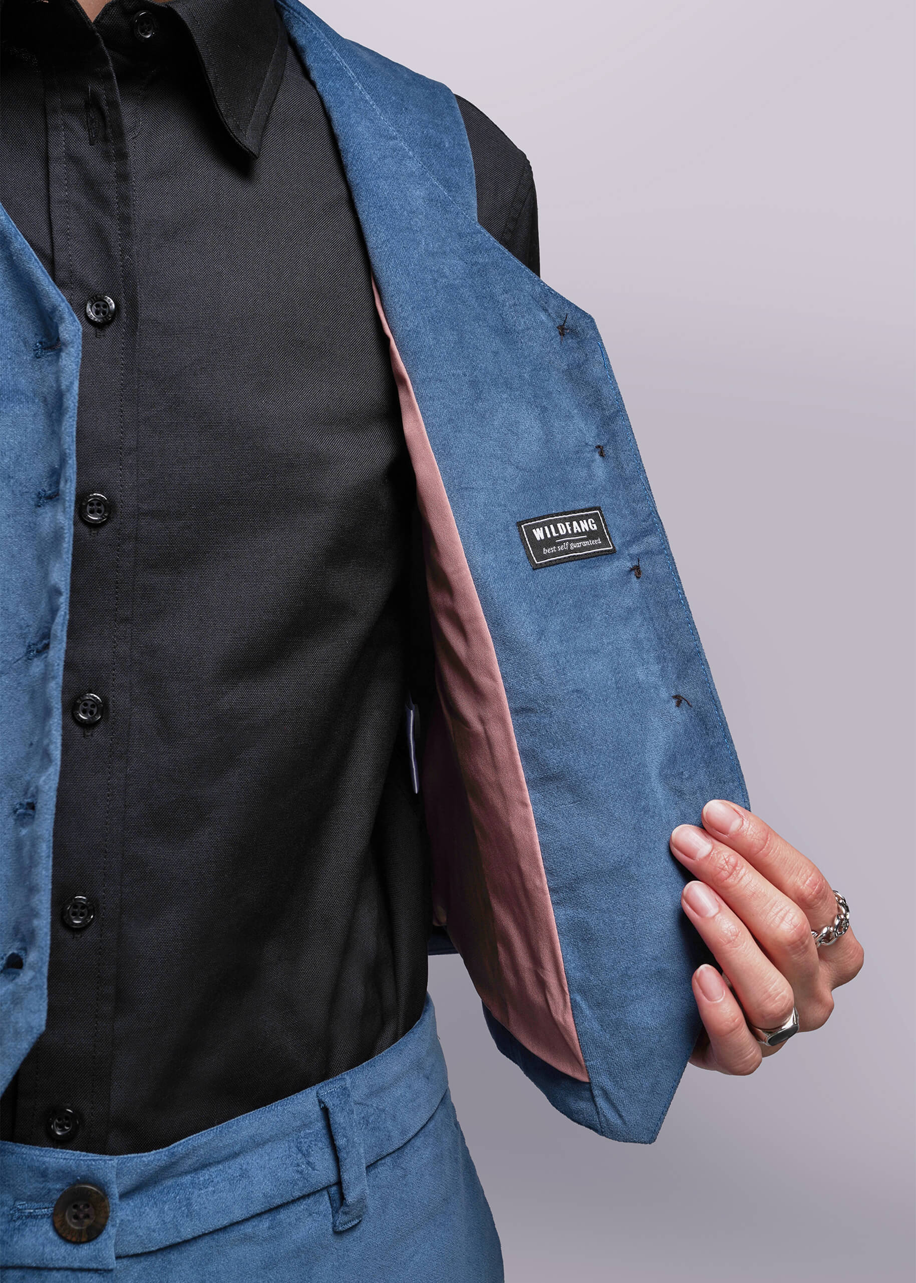 S=Close-up of a person wearing a blue vest with a visible brand label on a plain background