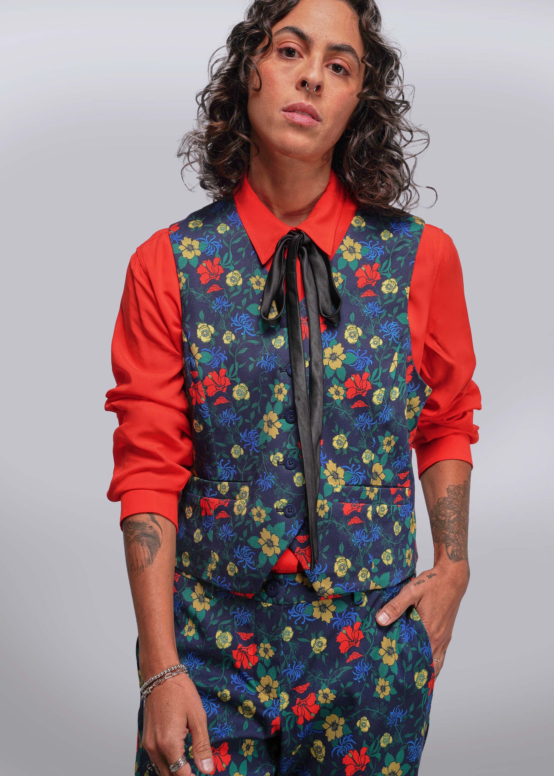 S=Person wearing a colorful floral vest over a red shirt with a plain background