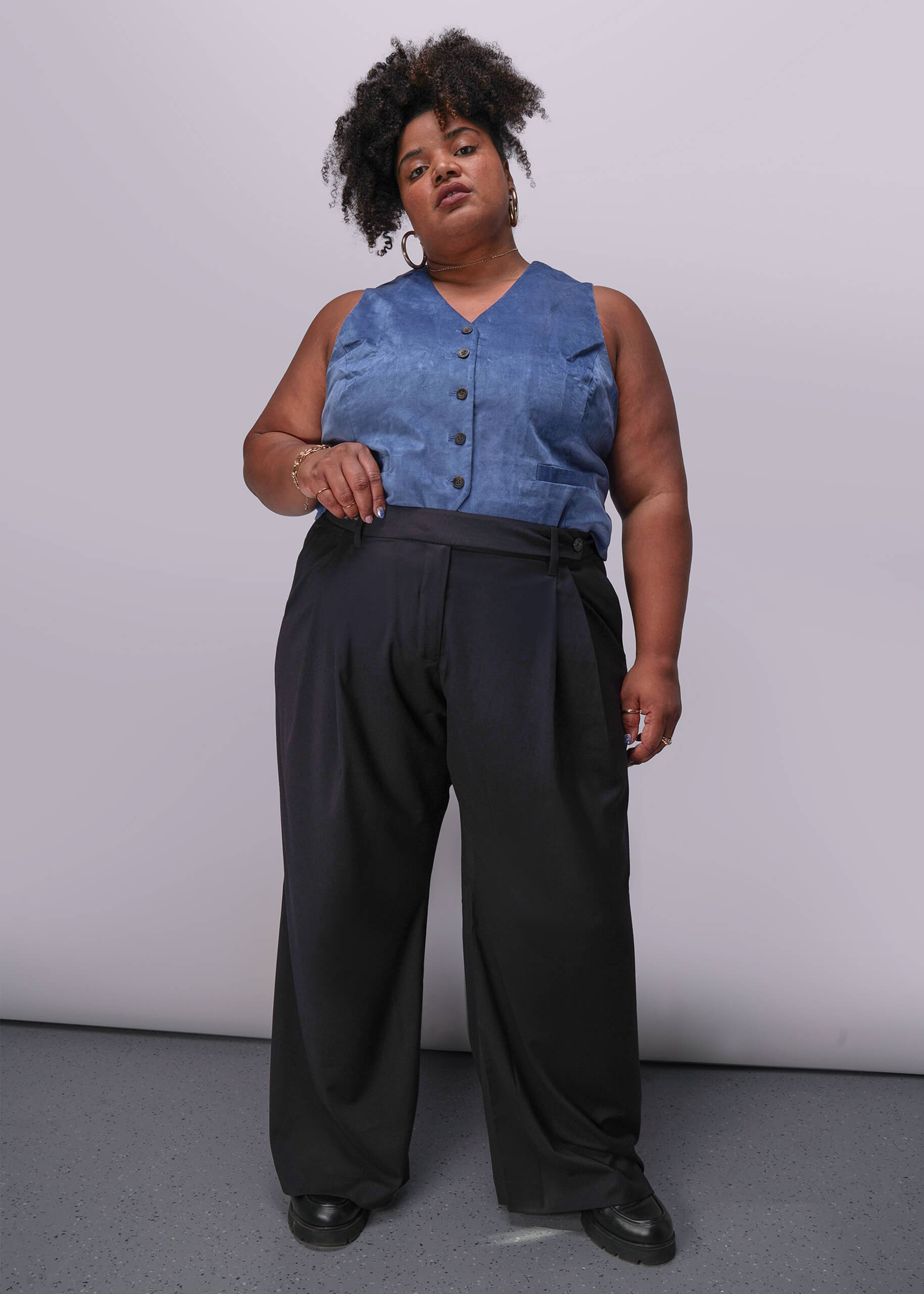 1X=Person wearing a blue sleeveless top and black pants against a plain background