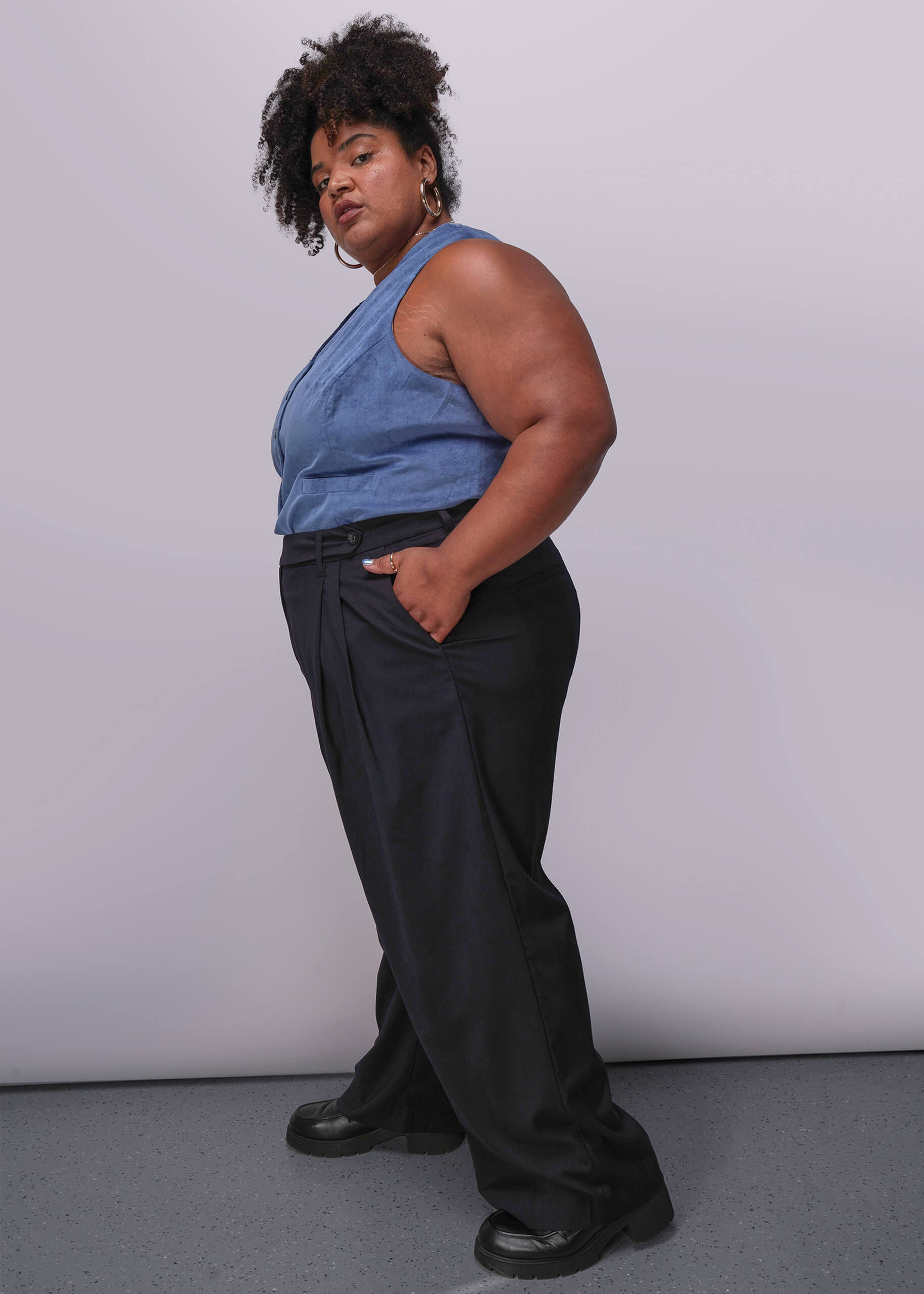 1X=Person wearing a blue sleeveless top and black pants against a plain background