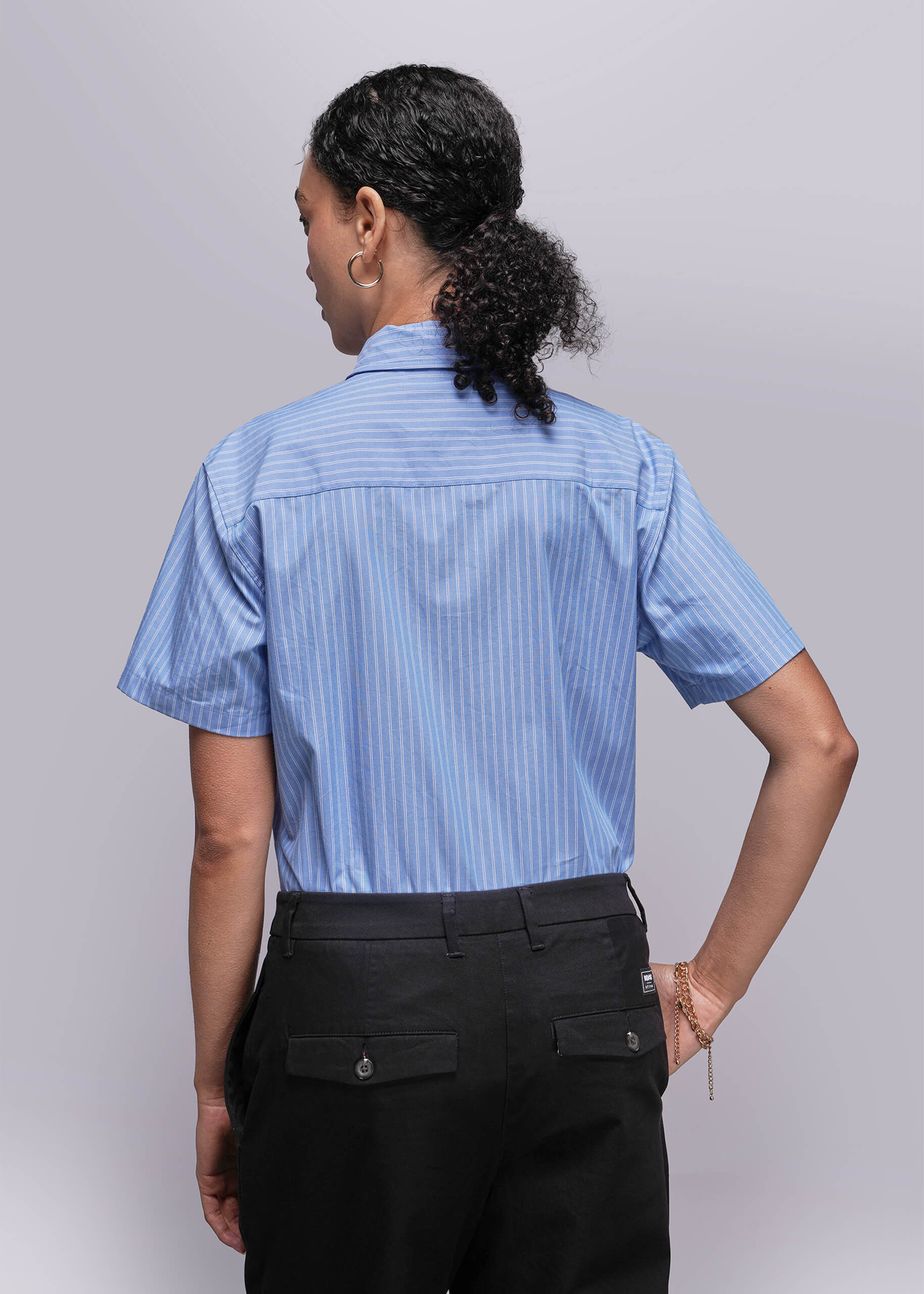 S=Back view of person wearing a blue striped shirt and black pants on a plain background