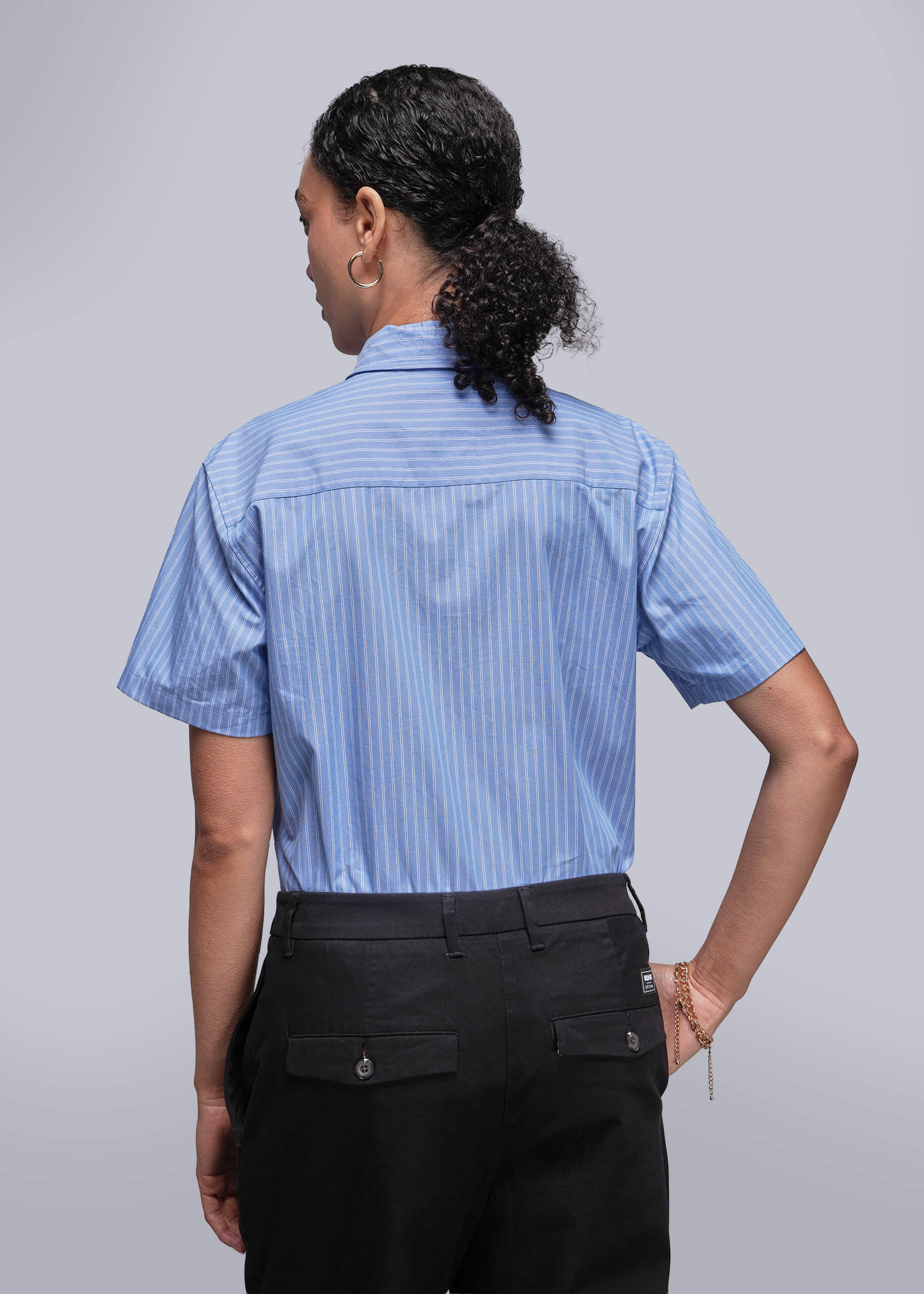 S=Back view of person wearing a blue striped shirt and black pants on a plain background