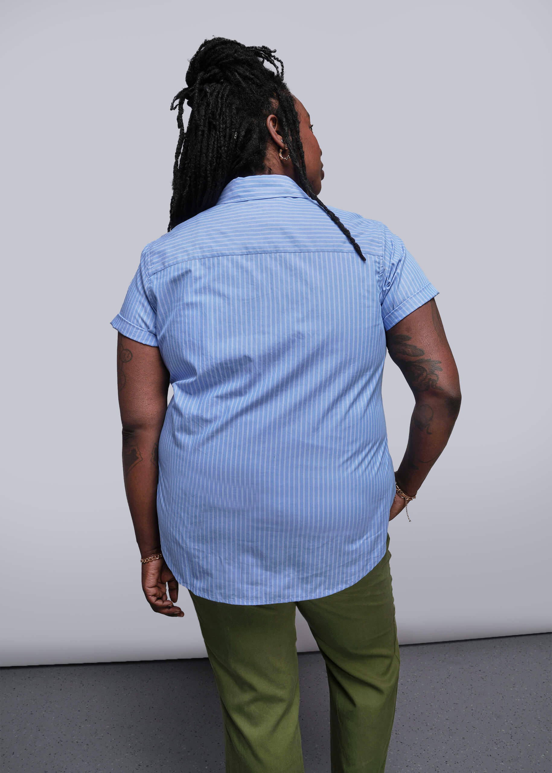 1X=Back view of person wearing a blue striped shirt and green pants against a plain background