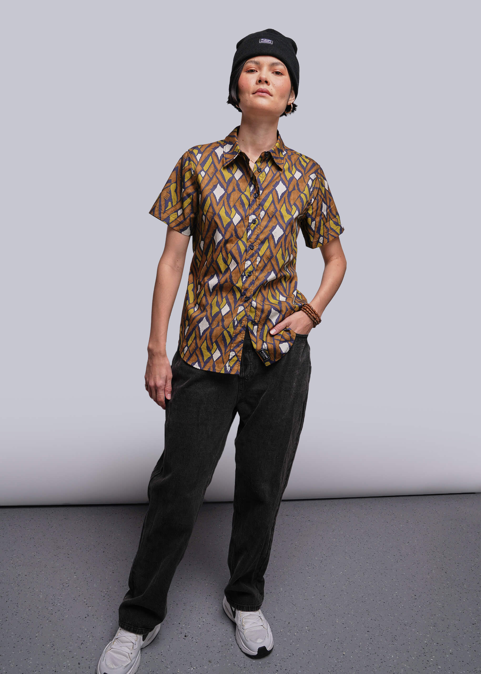 S=Person wearing a patterned shirt and black pants against a plain background