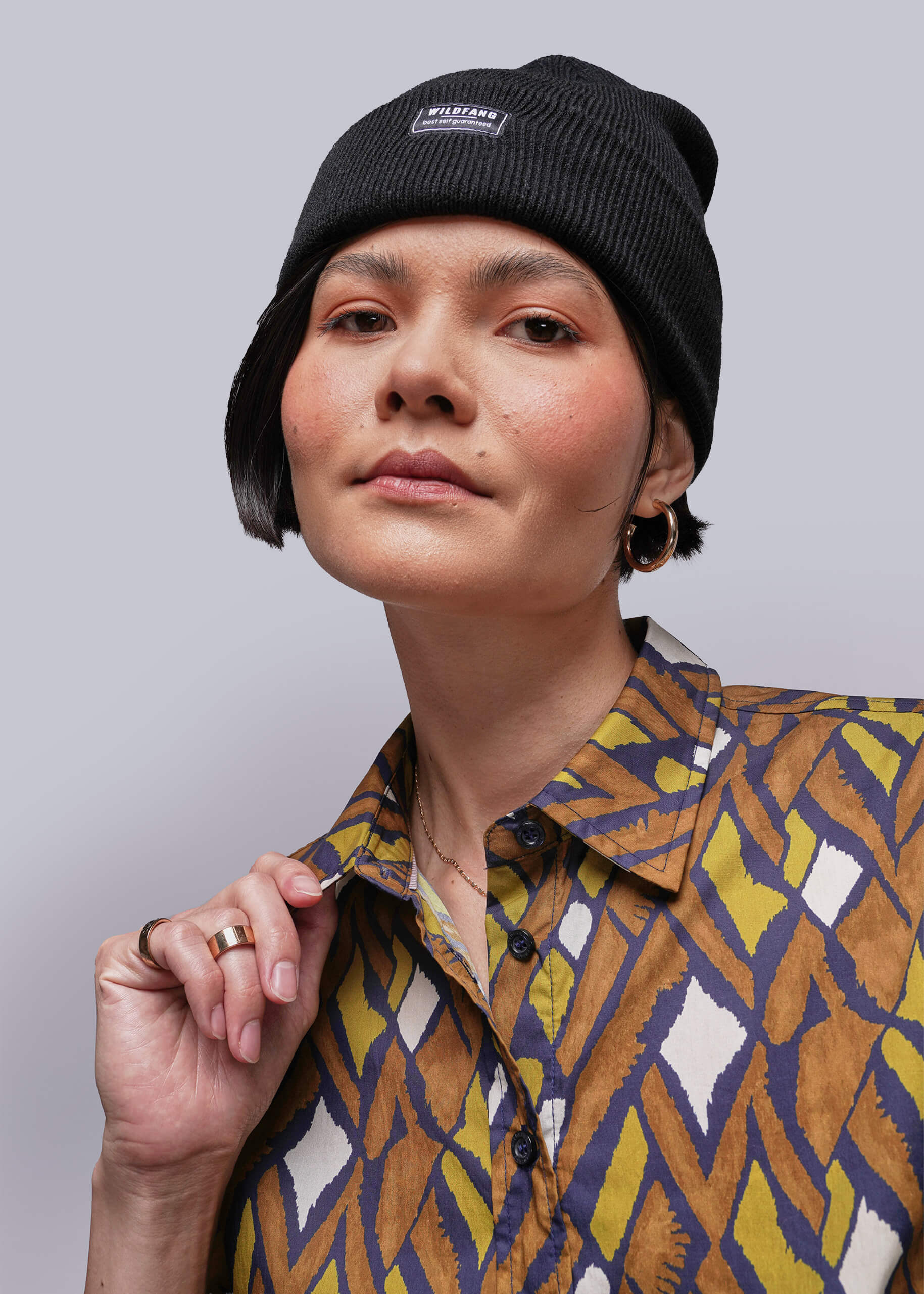 S=Person wearing a patterned shirt and black beanie with a visible brand logo on a gray background