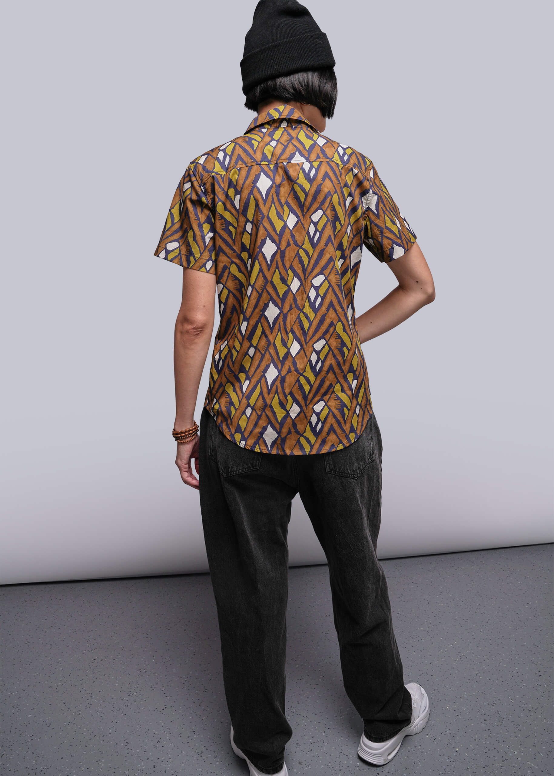 S=Person wearing a patterned shirt and black pants against a plain background
