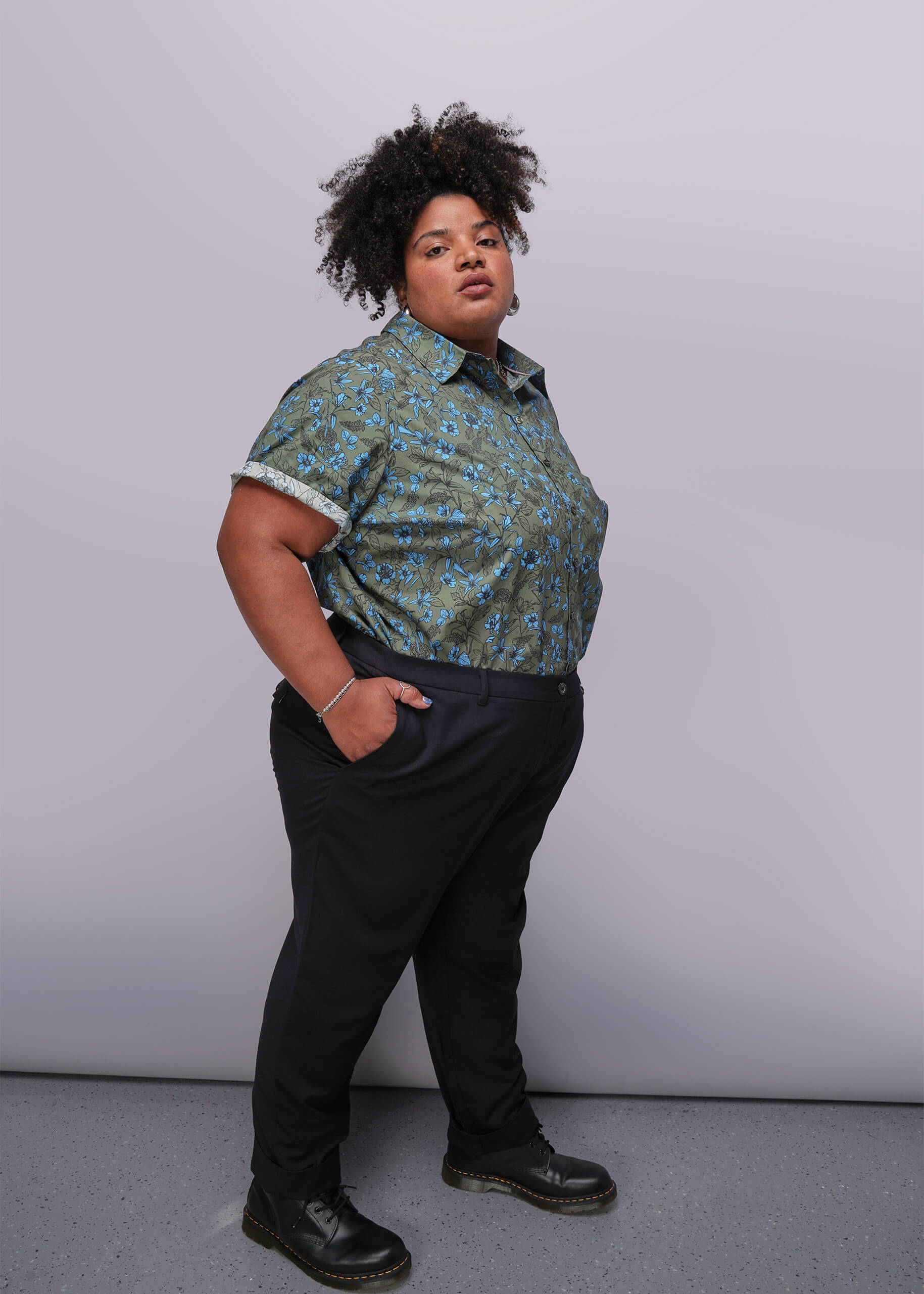 1X=Person wearing a patterned shirt and black pants against a plain background