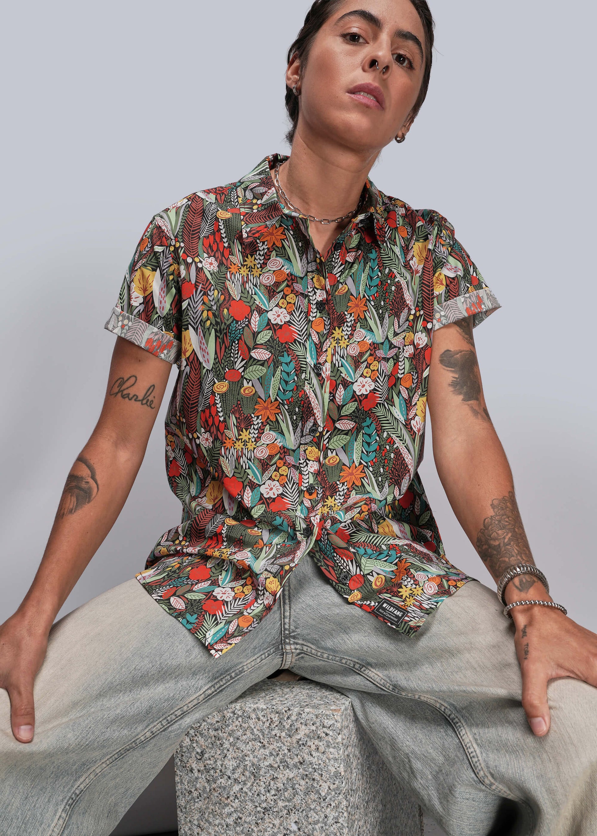 S=Person wearing a colorful floral shirt and light jeans against a plain background