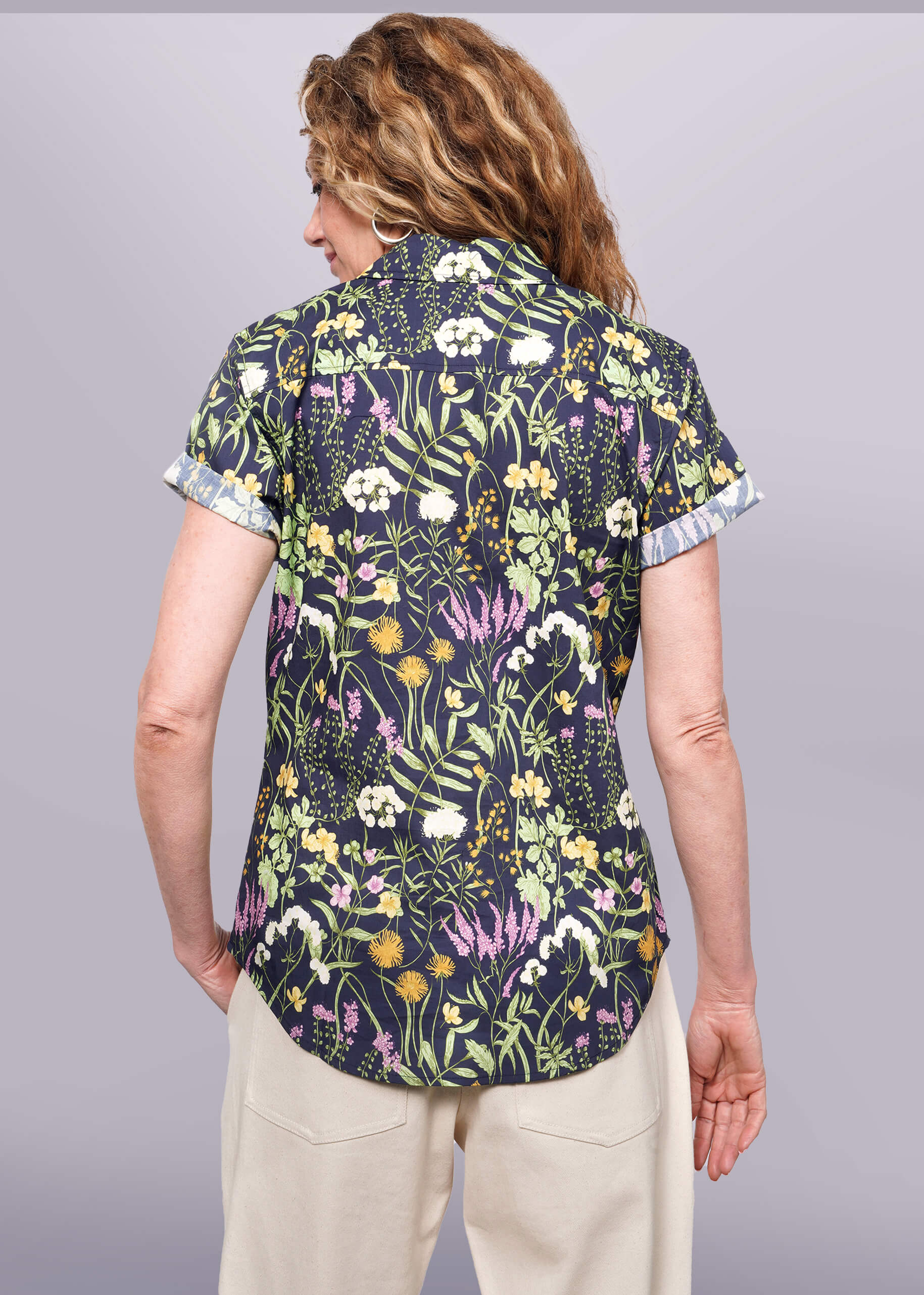 S= Back view of person with wavy blonde wearing short sleeve botanical printed button up shirt.