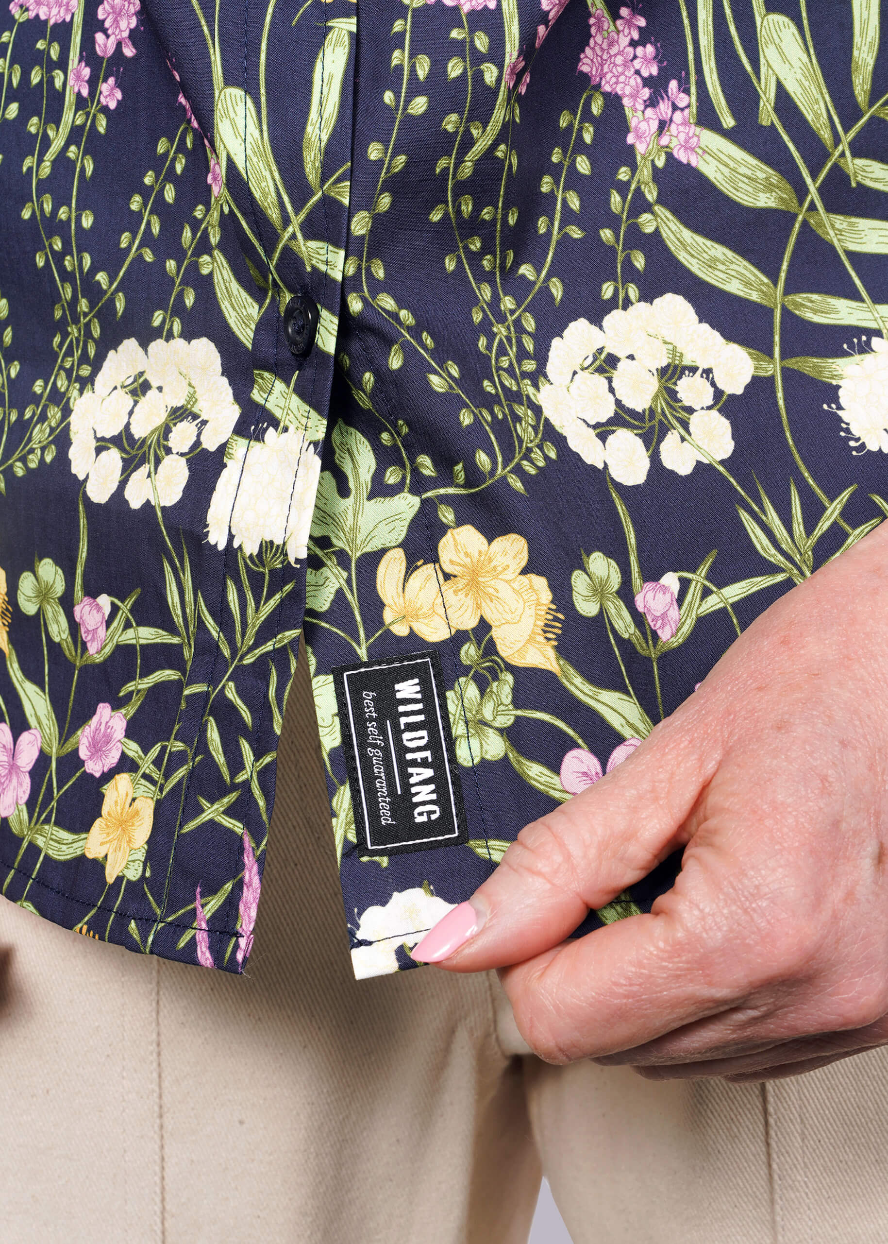 S=Close up of person holding bottom hem of botanical printed shirt showing WILDFANG label.