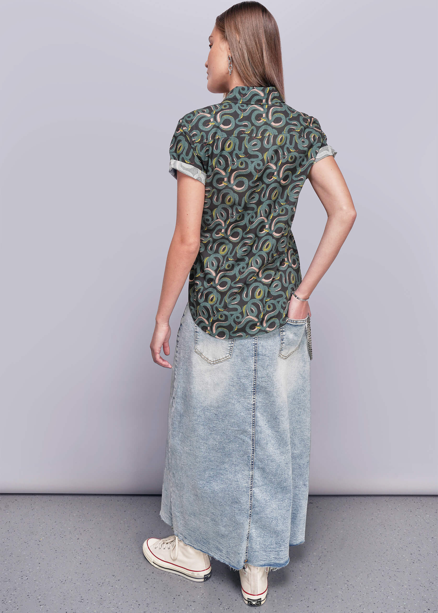 S=Person wearing a patterned shirt and denim skirt on a plain background