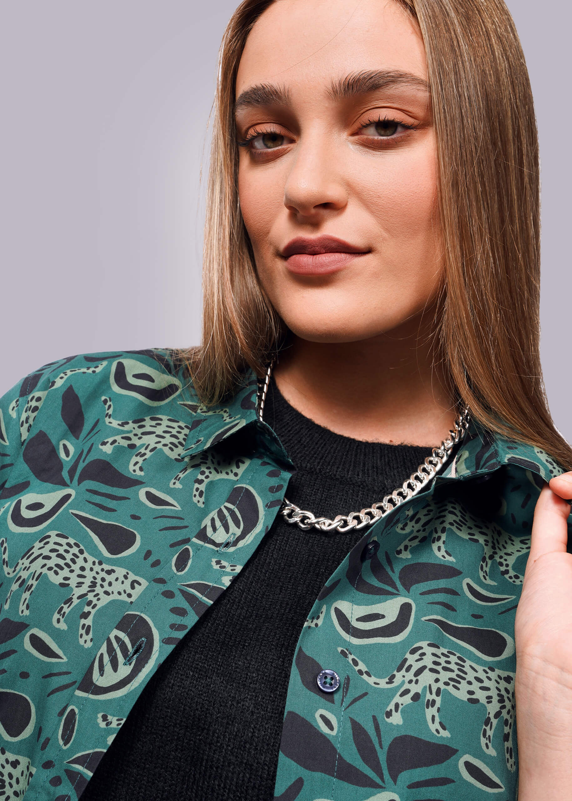 S= A person with long hair wears a green abstract-patterned The Essential Button Up from Wildfang over a black top. They slightly pull the collar to showcase a thick silver chain necklace. Made from breathable cotton, it features a modern tailored fit against a simple white gradient backdrop.