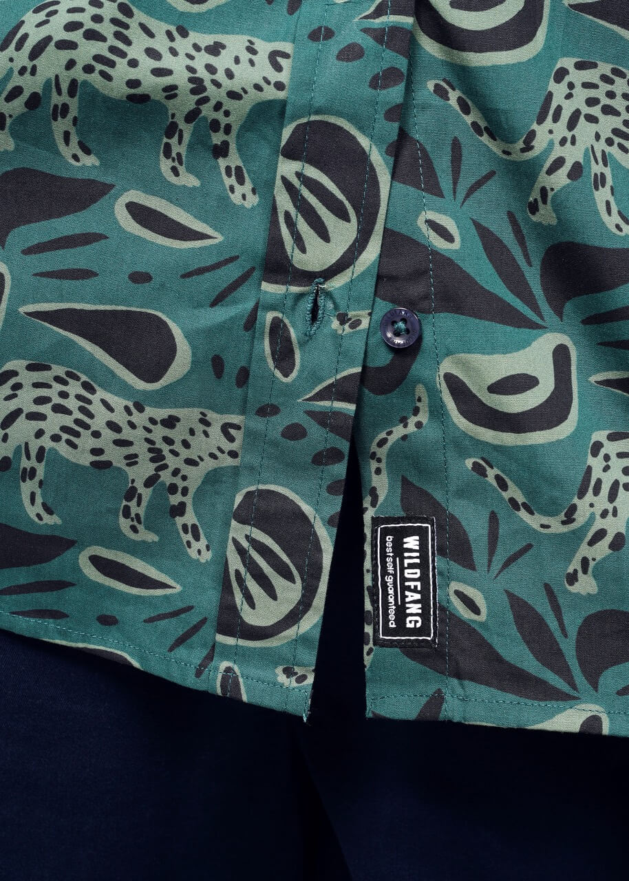 1X=The Essential Button Up by Wildfang features a tailored fit with green abstract animal designs in black and light green on breathable cotton. It has black buttons and a visible WILDFANG label near the hem, styled perfectly over dark pants.