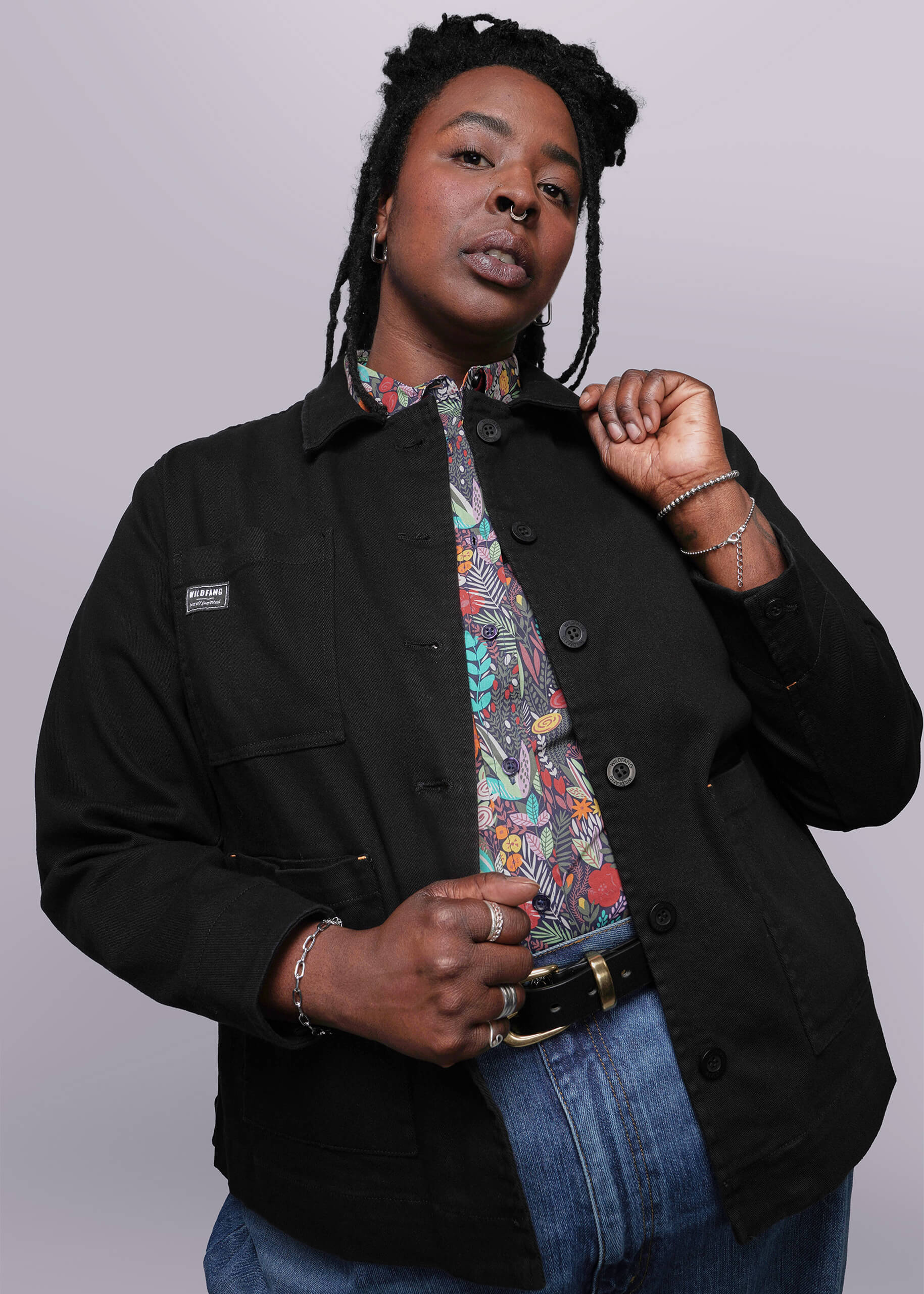 1X=Person wearing a black jacket over a colorful shirt with a plain background