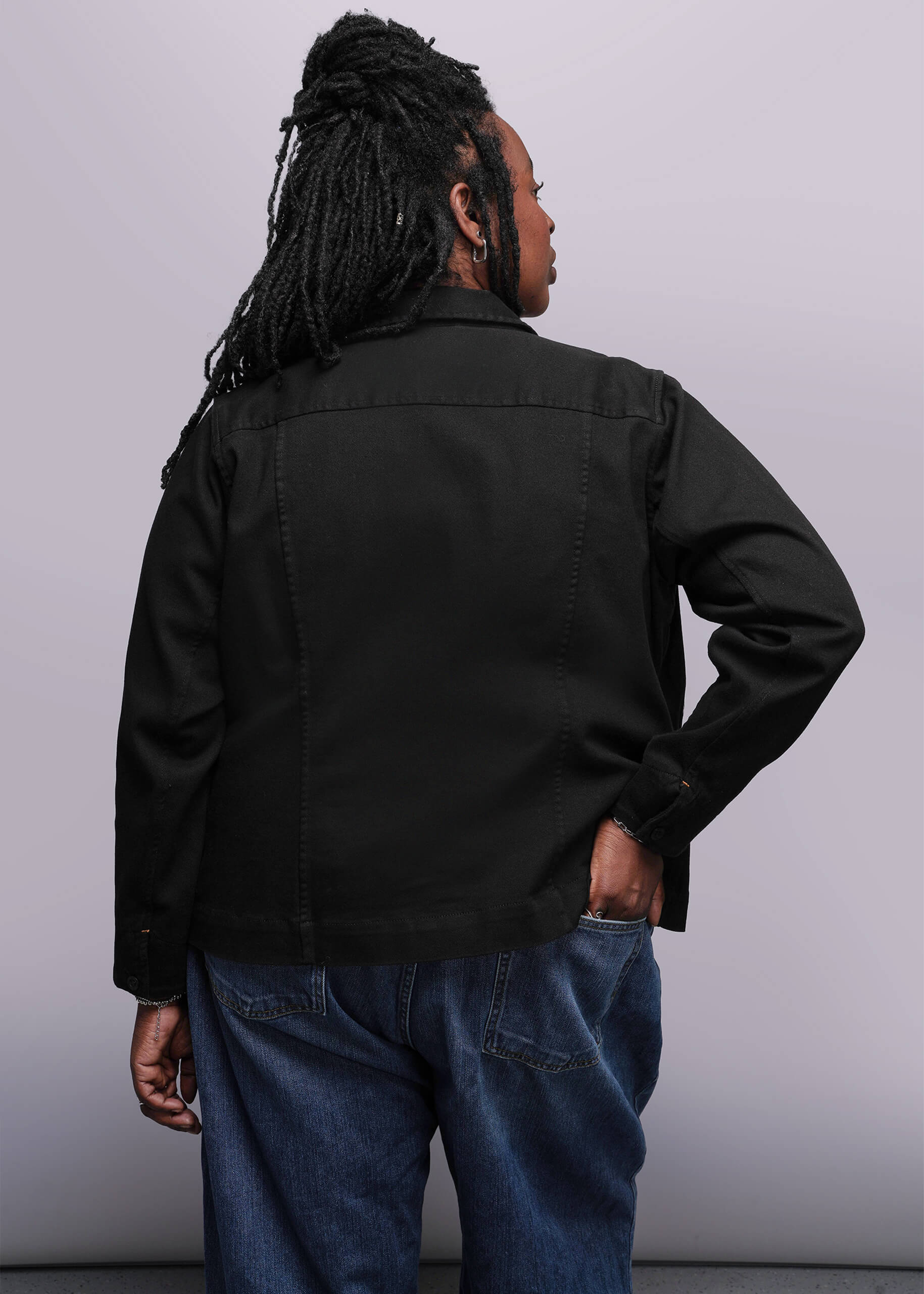 1X=Person wearing a black denim jacket and blue jeans against a plain background