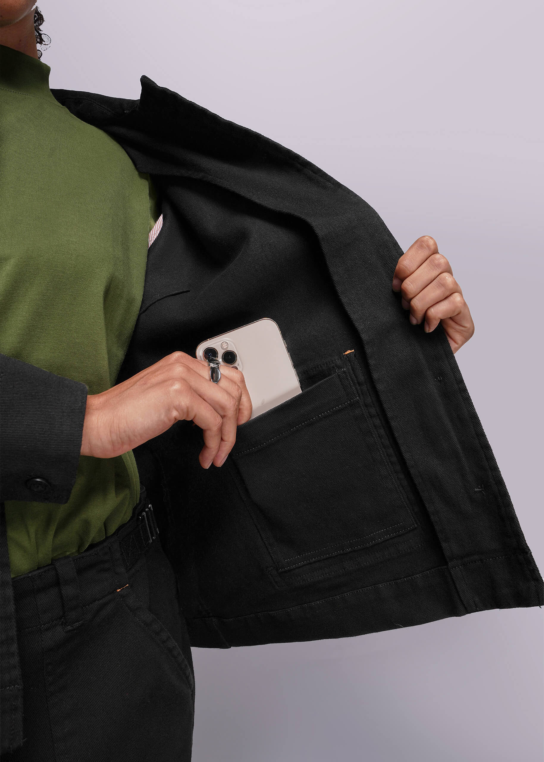 S=Person wearing a black jacket with a white phone in the pocket against a light gray background