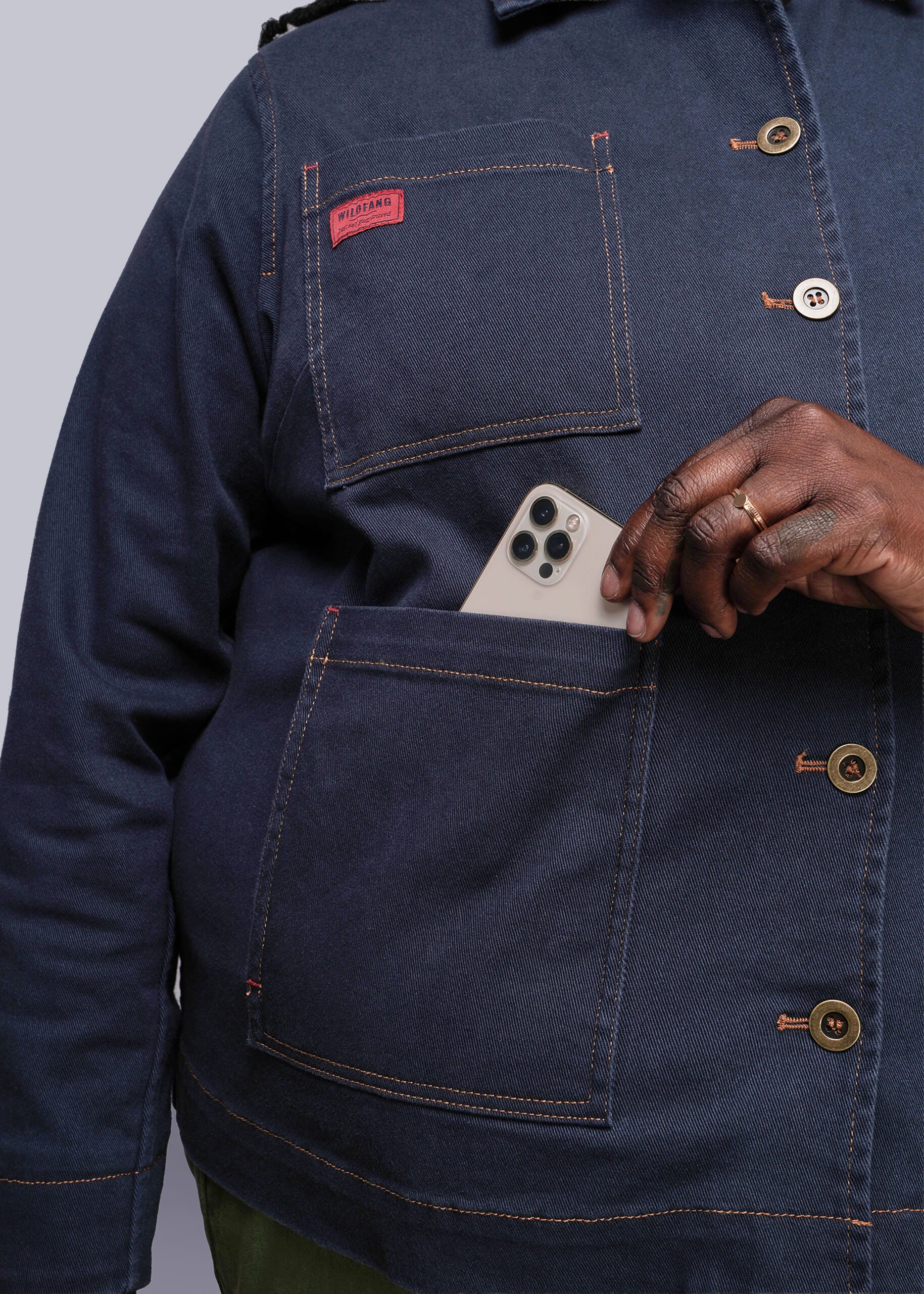 1X=Person wearing a blue jacket with a phone in the pocket against a gray background