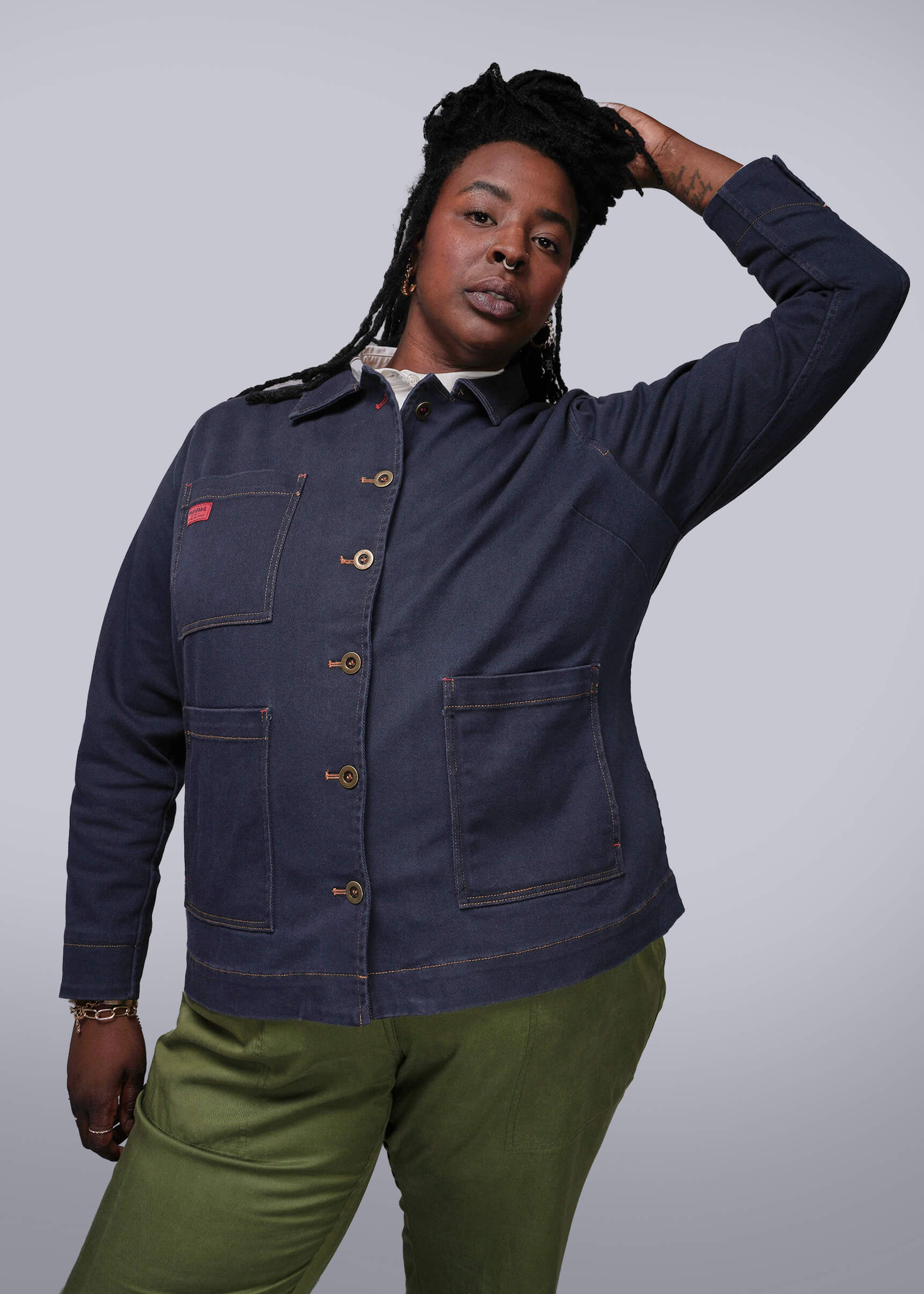 1X=Person wearing a navy blue jacket with a white shirt underneath, standing against a plain background.