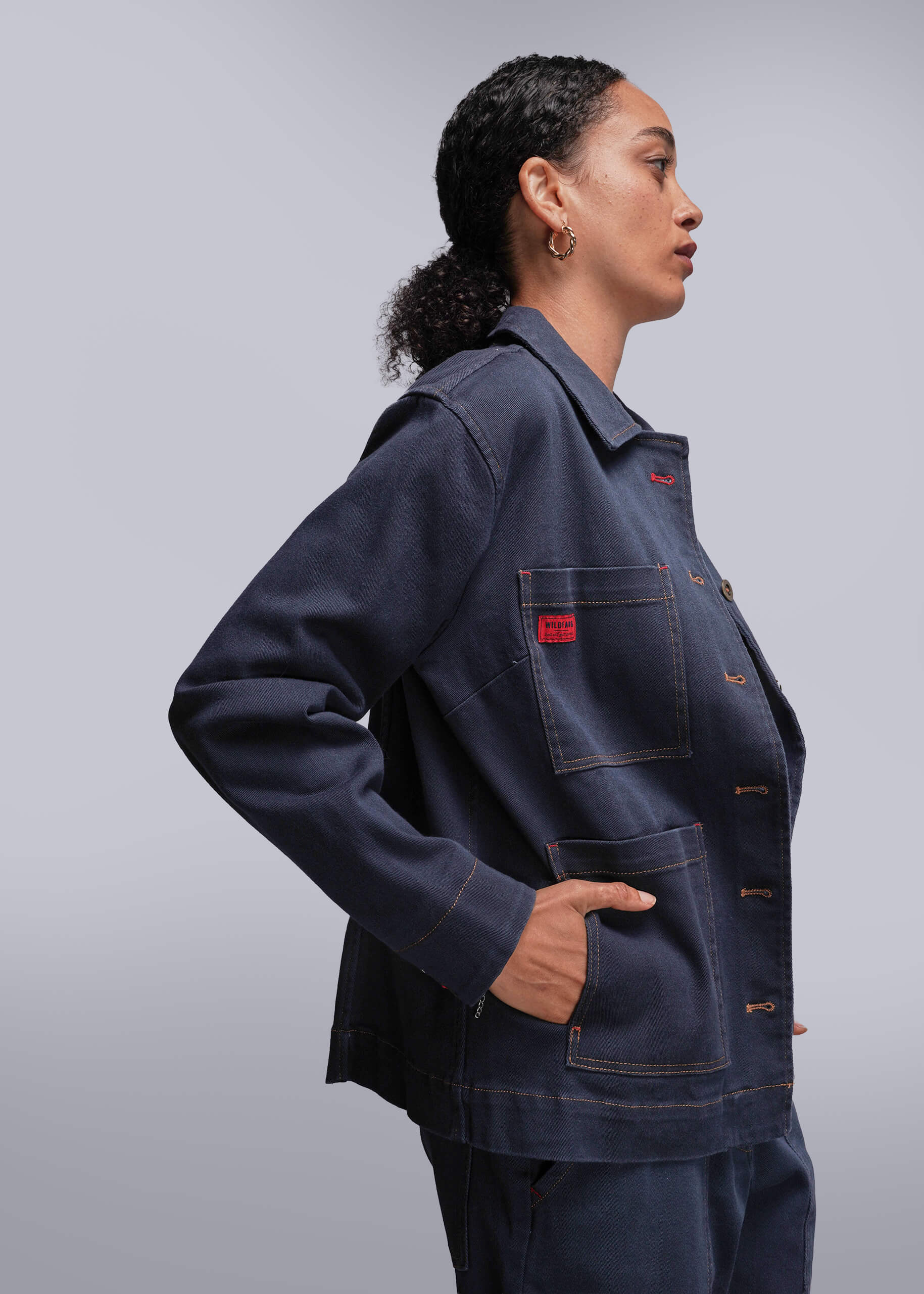 S=Person wearing a dark denim jacket with red accents on a light gray background