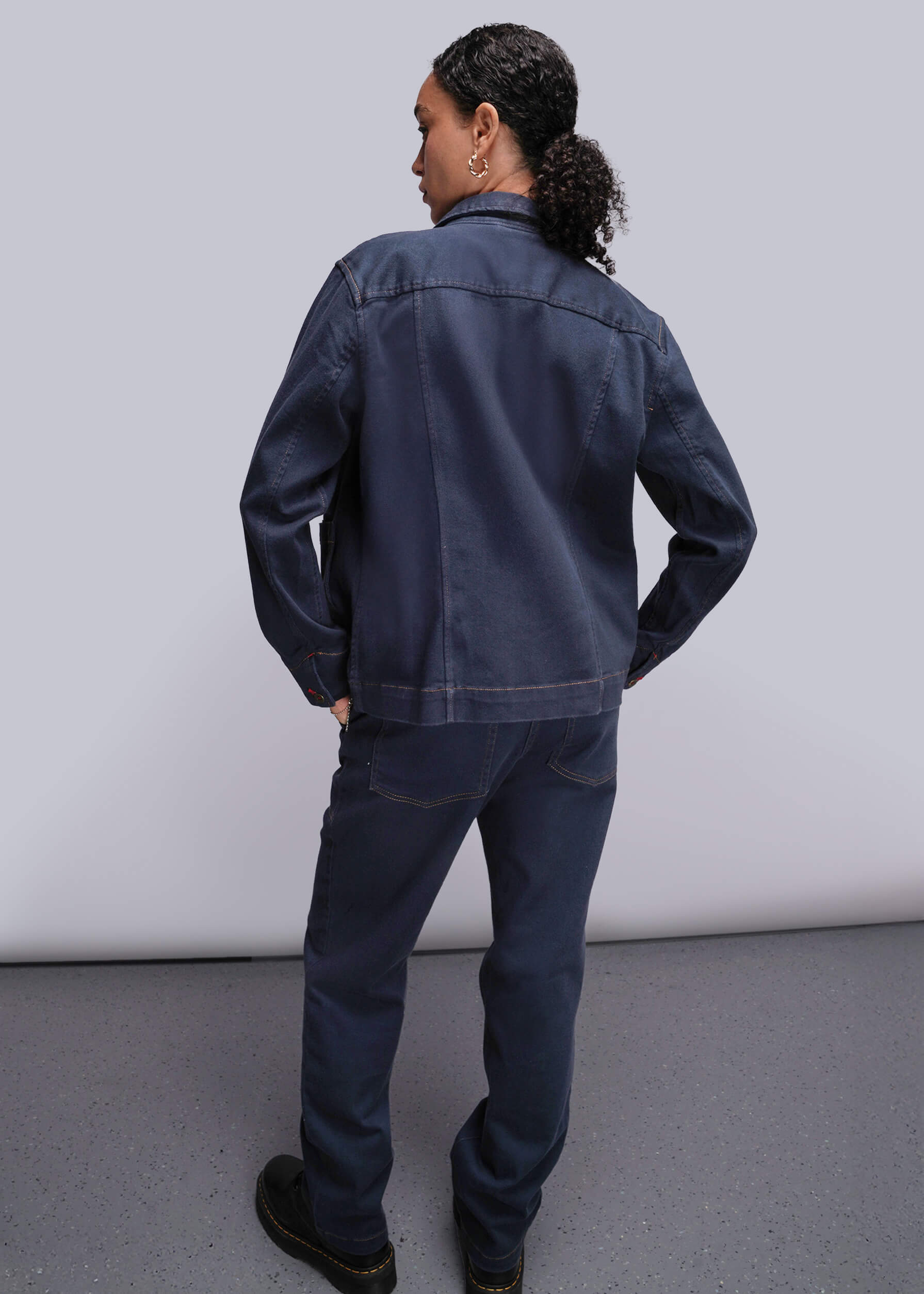 S=Person wearing a dark blue denim jacket and pants against a plain background