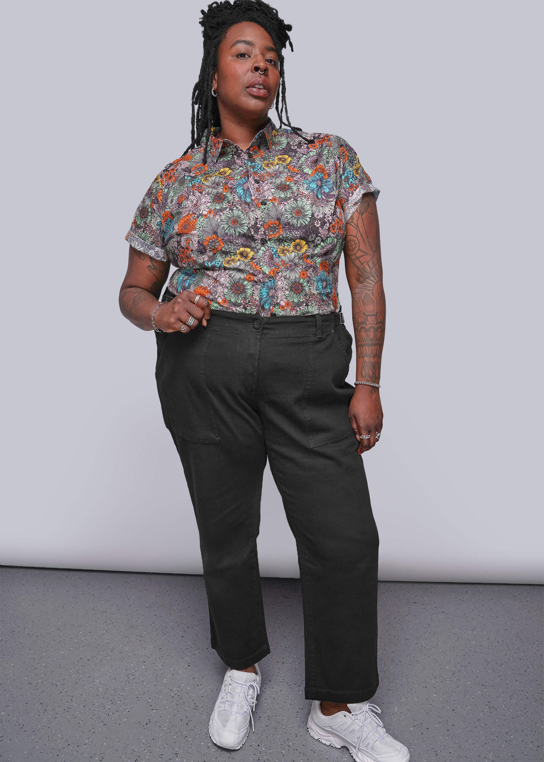 1X=Person wearing a colorful floral shirt and black pants against a plain background