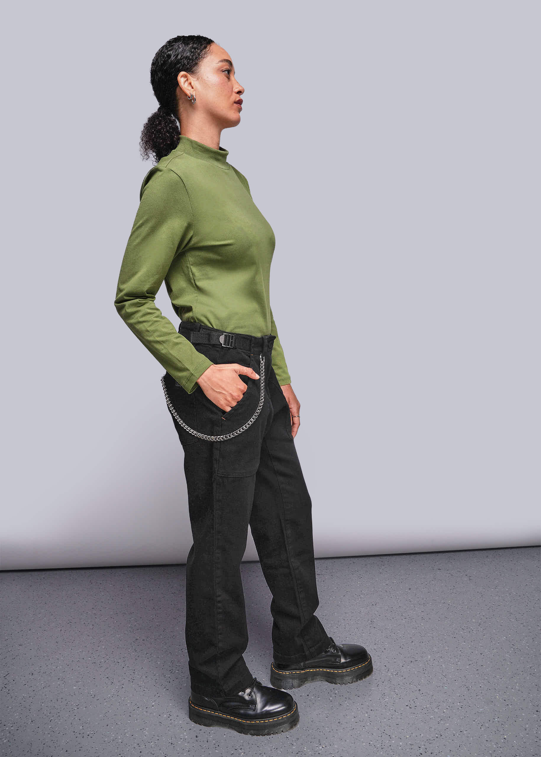 S=Person wearing a green shirt and black pants against a plain background