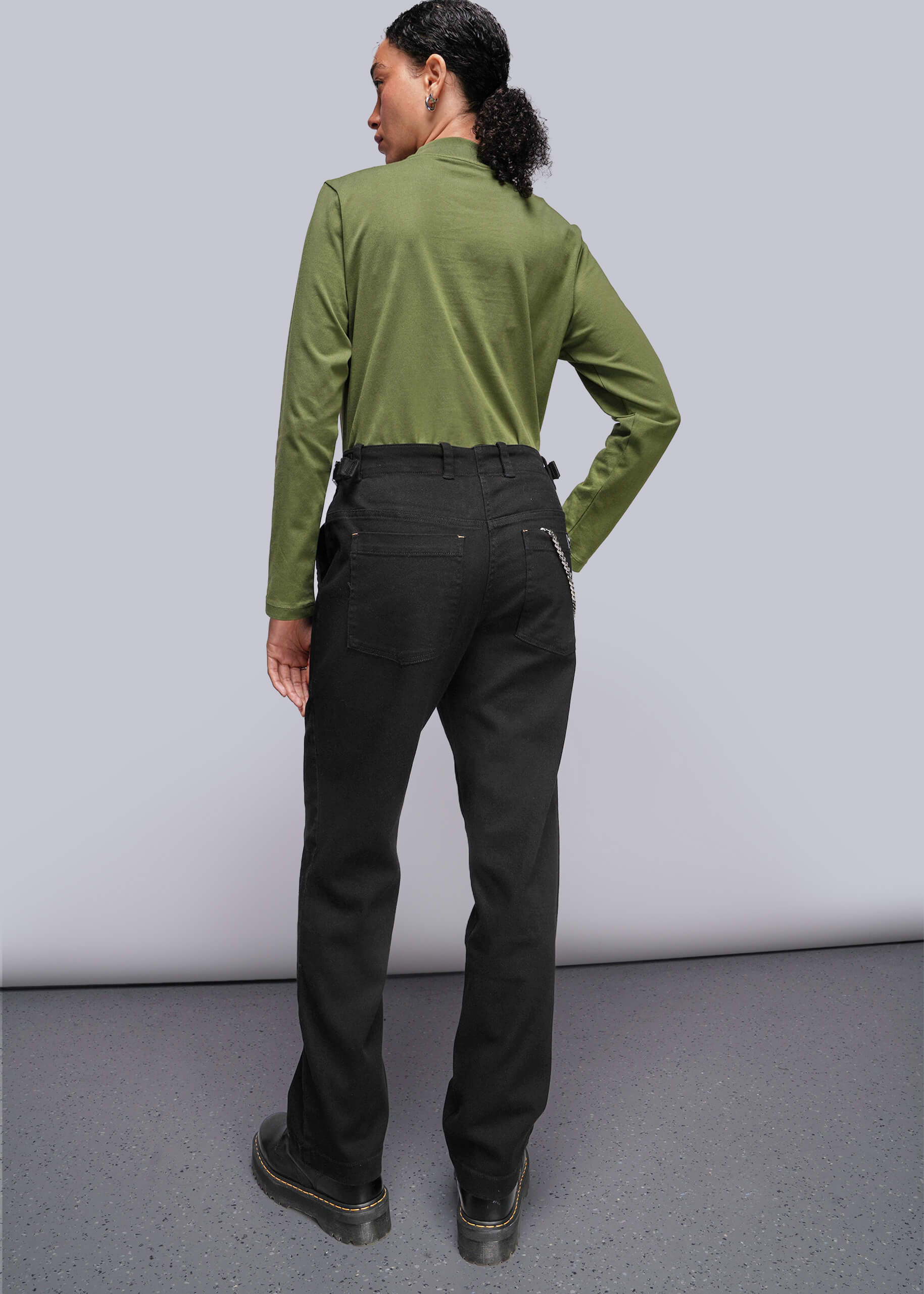 S=Person wearing a green shirt and black pants against a plain background