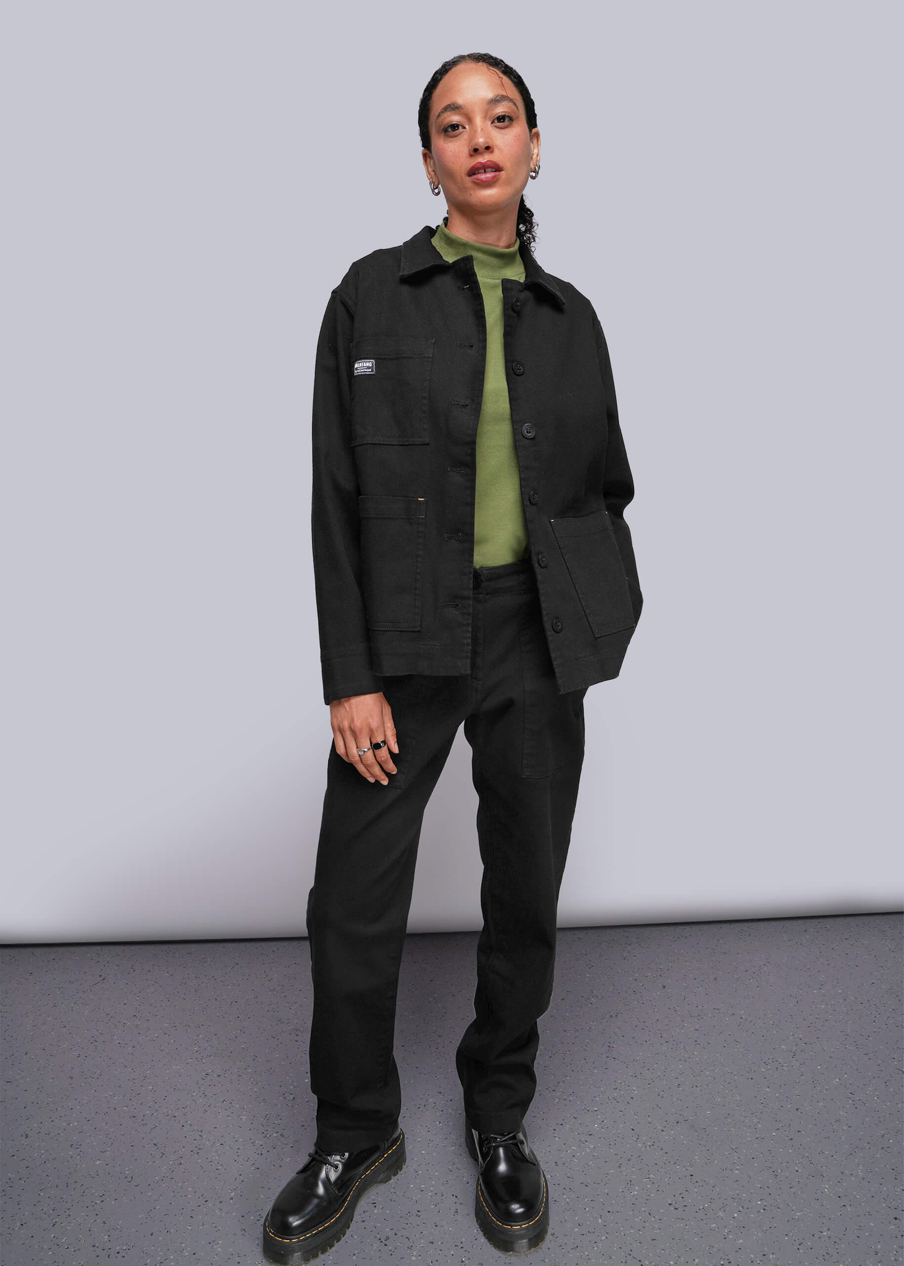 S=Person wearing a black jacket and pants with a green shirt underneath against a plain background