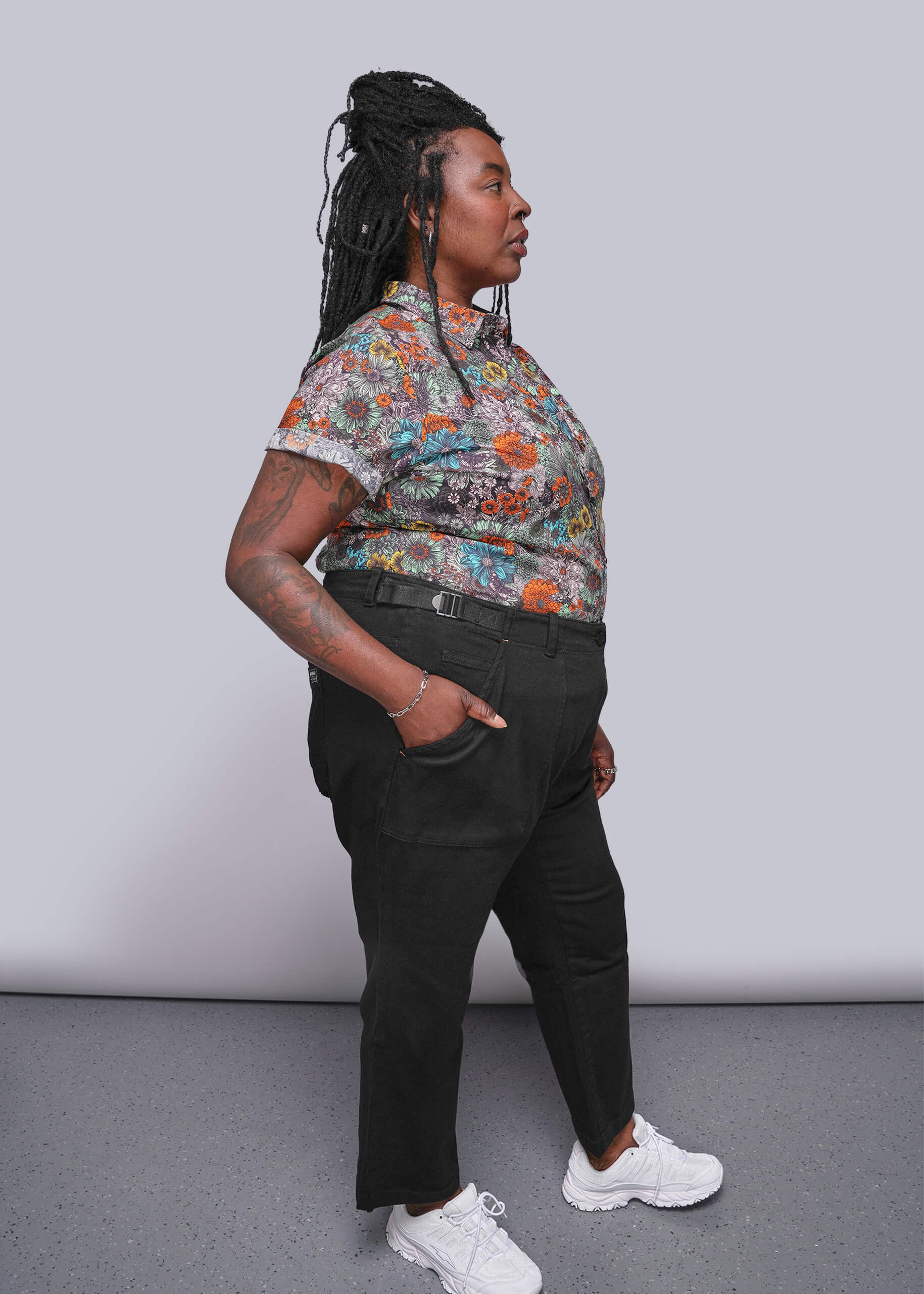 1X=Person wearing a colorful floral shirt and black pants against a plain background