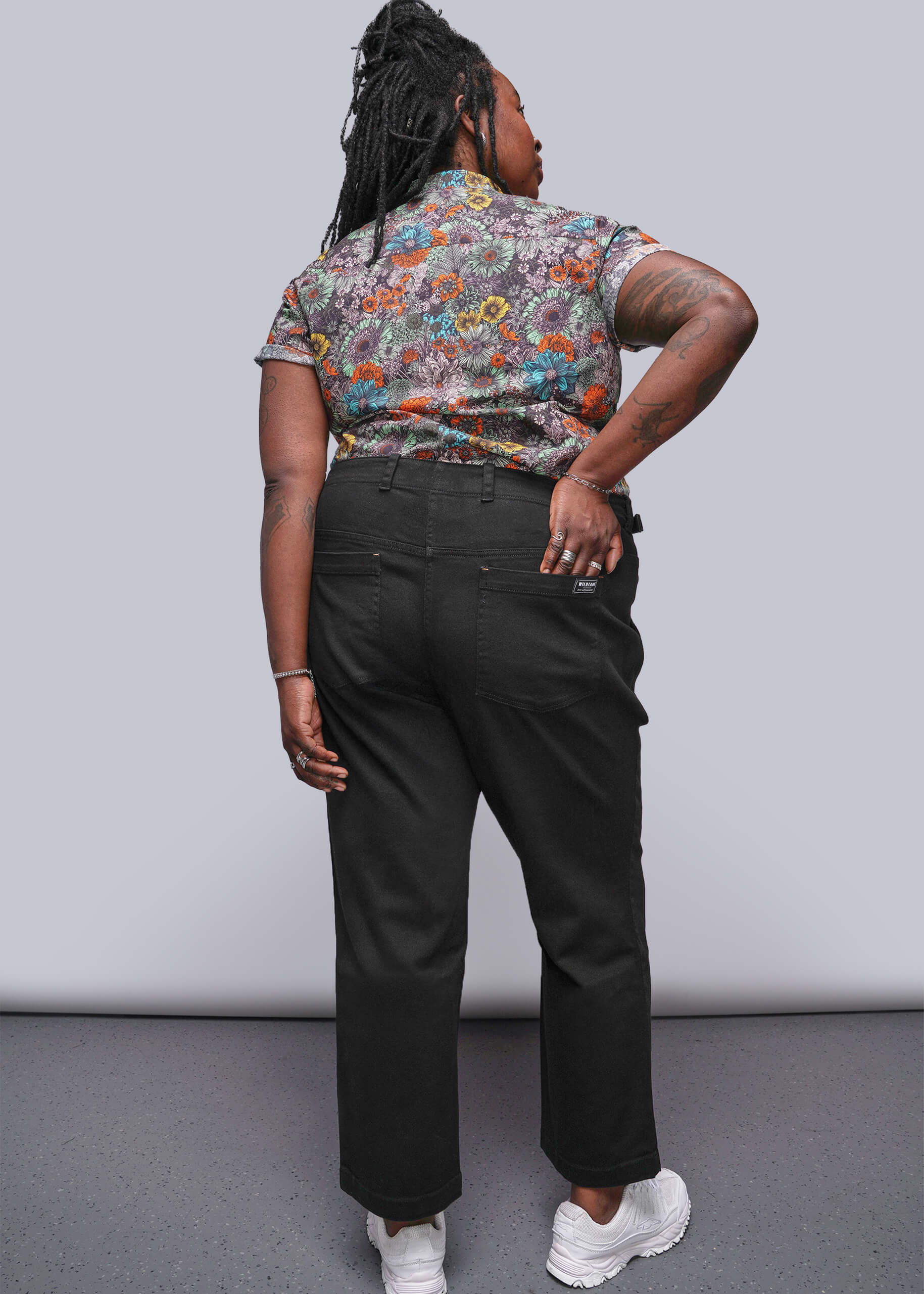 1X=Person wearing a colorful floral shirt and black pants against a plain background