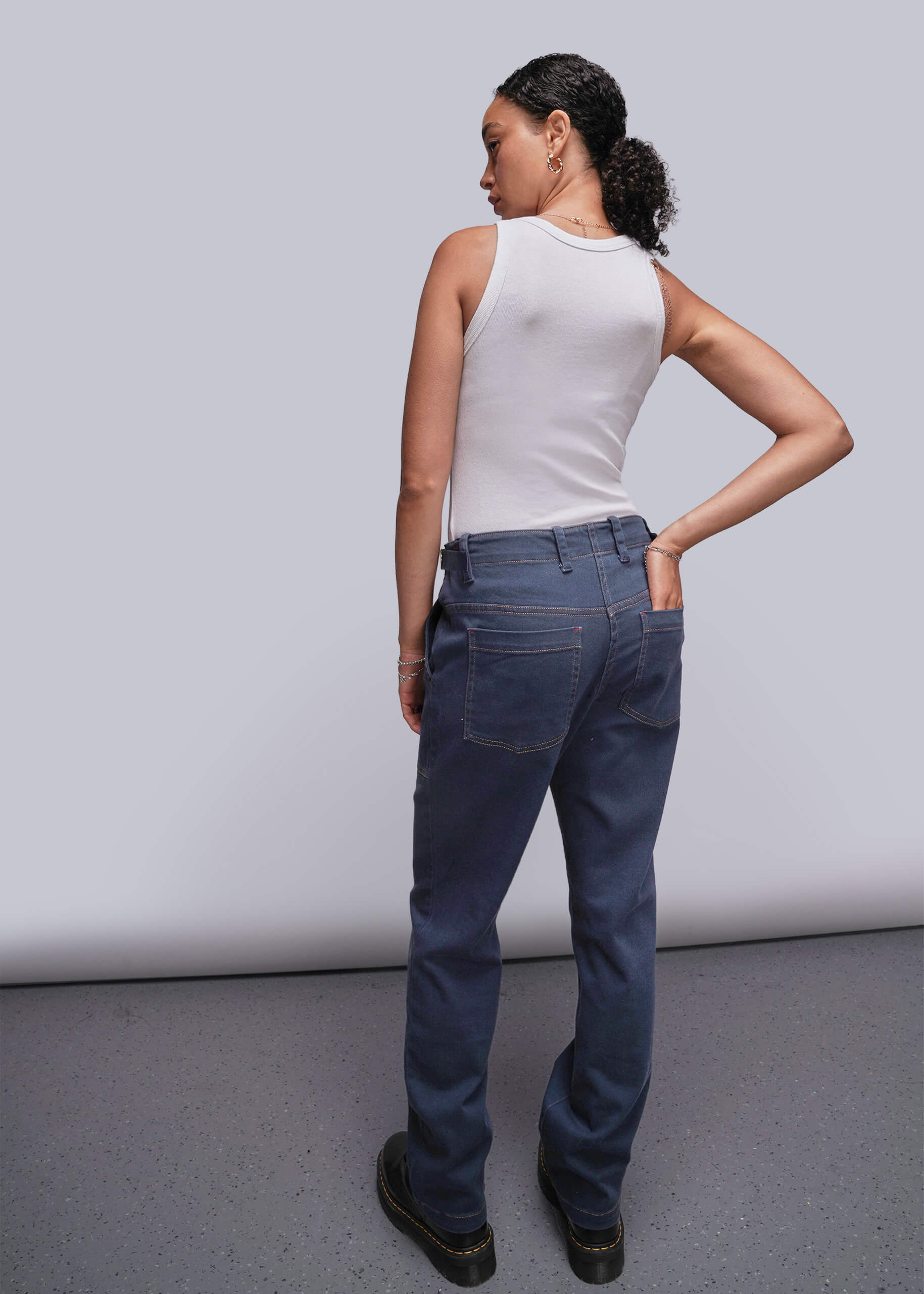 S=Person wearing a white sleeveless top and dark blue jeans against a plain background