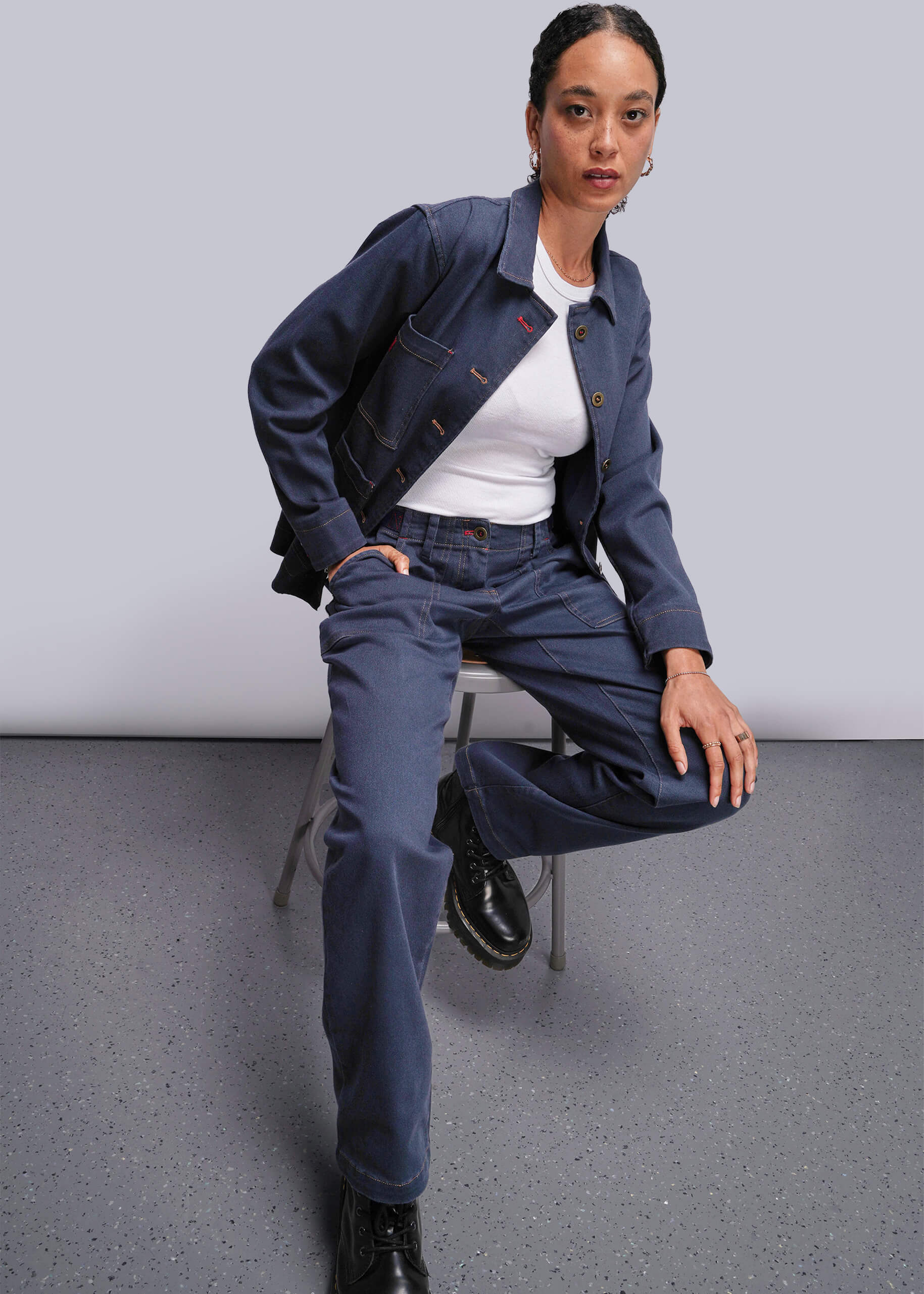 S=Person wearing a navy jacket and pants sitting on a chair against a plain background