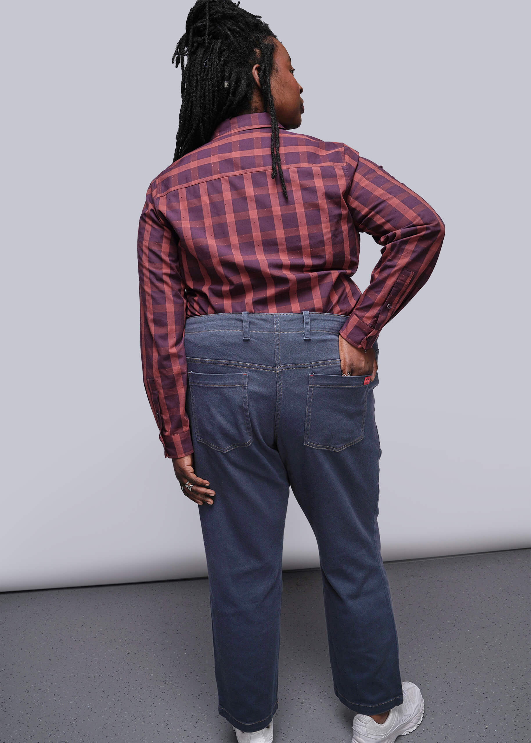 1X=Person wearing a red and black plaid shirt and blue jeans against a plain background
