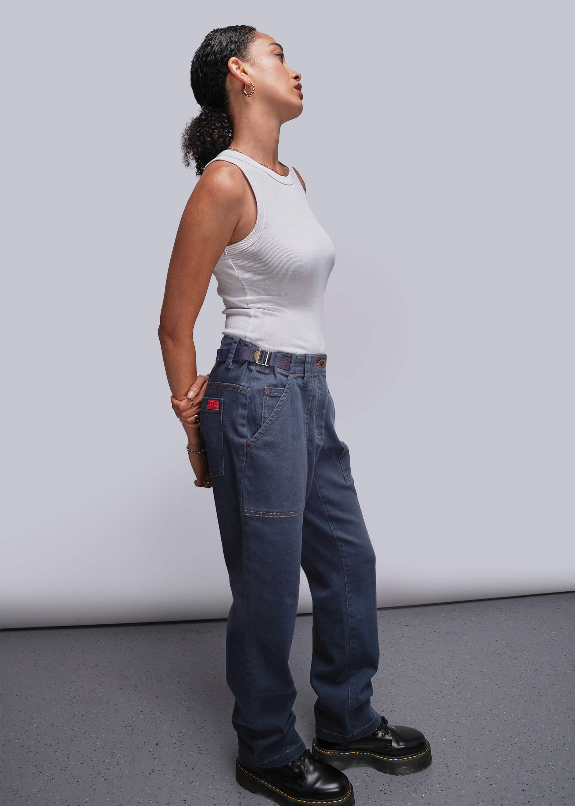 S=Person wearing a white tank top and blue jeans against a plain background