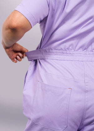 1X=A person in The Essential High Waisted Coverall adjusts the back waist strap, showcasing the elastic high-waisted fit and single back pocket. The image highlights their back and arm, emphasizing comfort and adjustability.