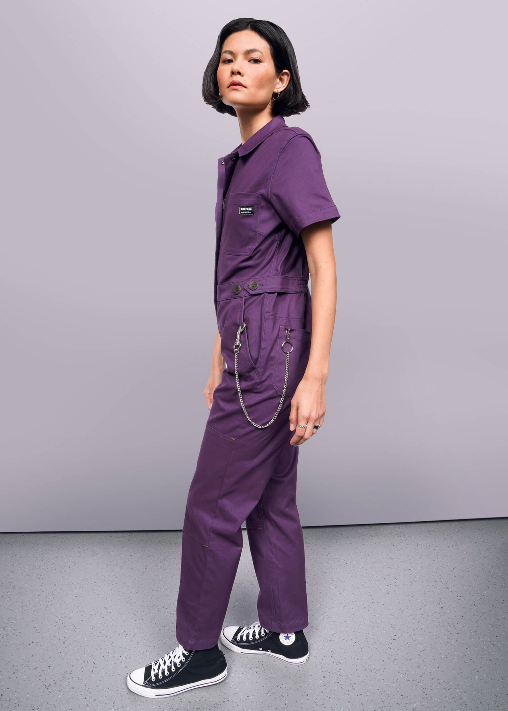 S=Person wearing a purple jumpsuit with black shoes on a gray background
