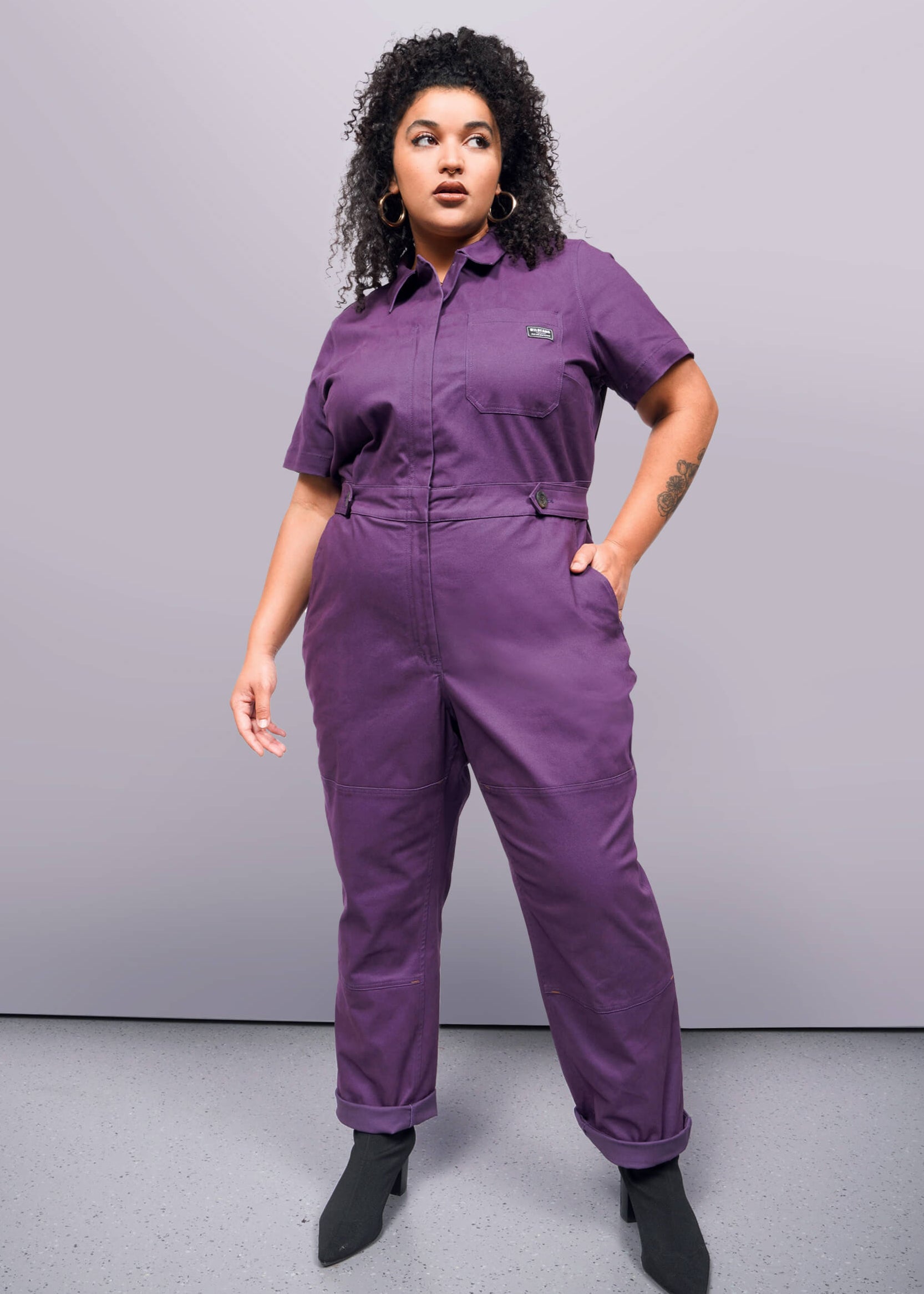 1X=Person wearing a purple jumpsuit against a gray background
