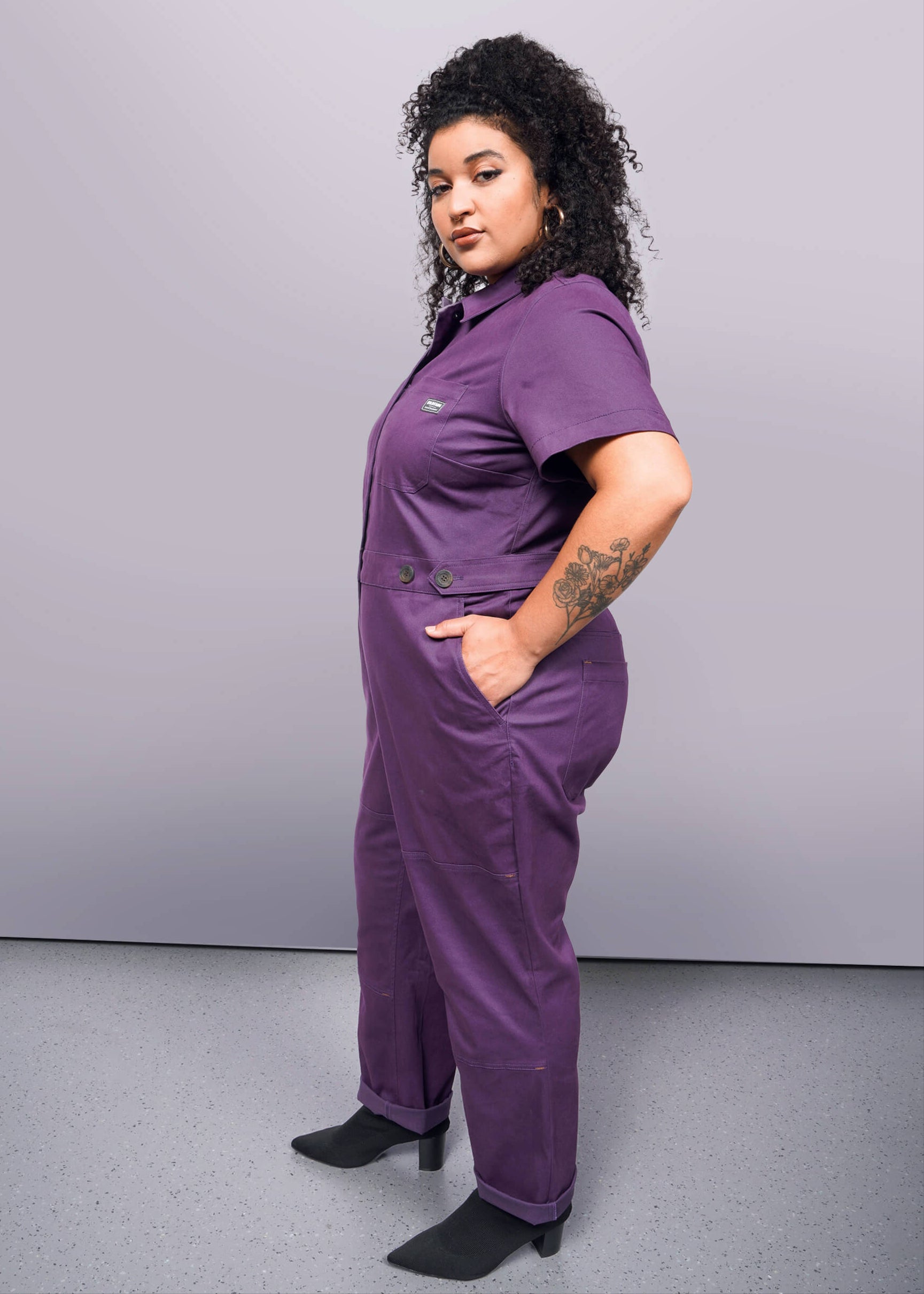 1X=Person wearing a purple jumpsuit against a plain background