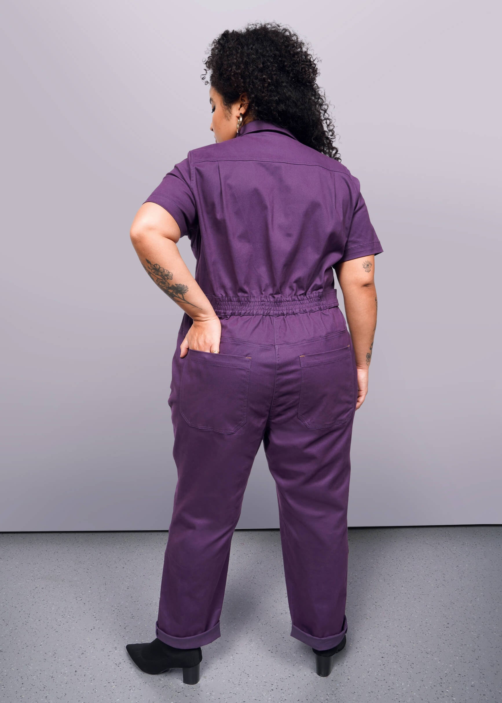 1X=Person wearing a purple jumpsuit against a gray background