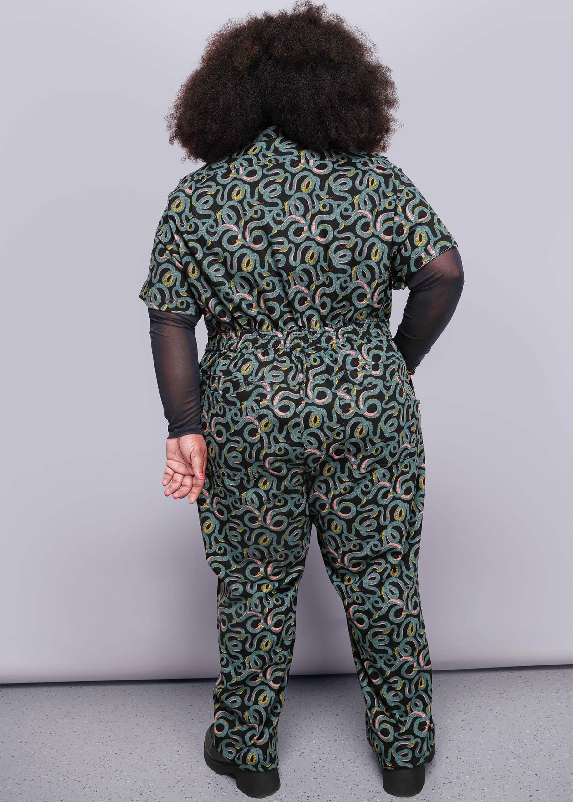 1X=Person wearing a patterned jumpsuit on a plain background