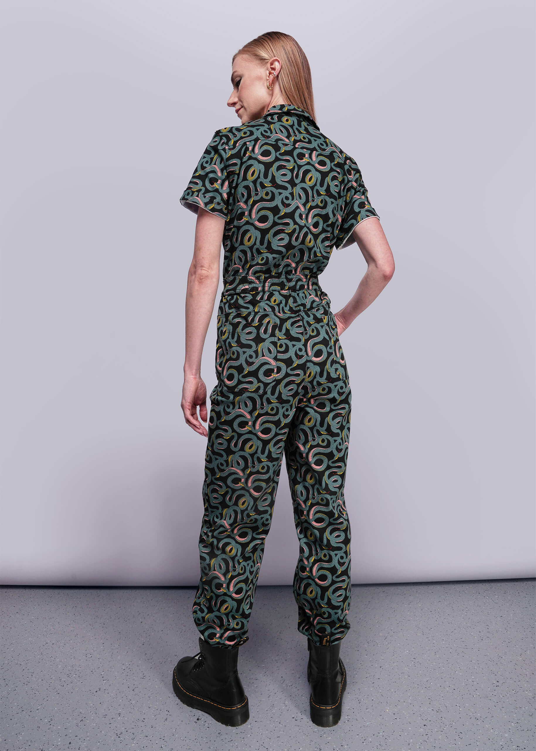 S=Person wearing a green patterned jumpsuit on a plain background